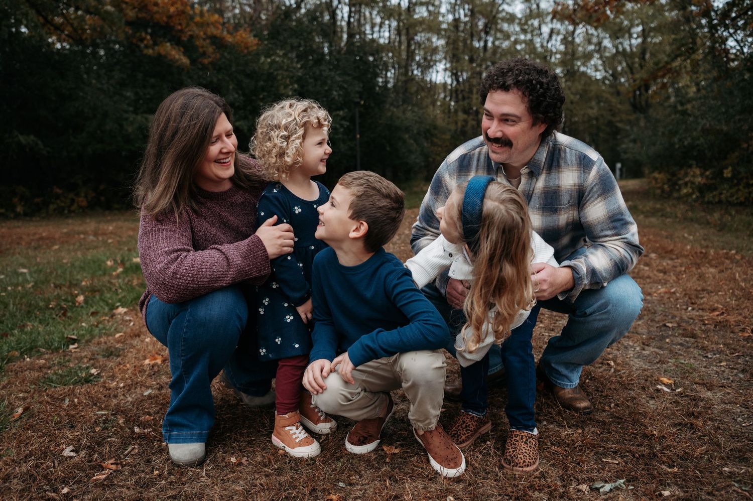 A smiling family of five crouches together in a colorful autumn forest setting.Bloomington, Minnesota