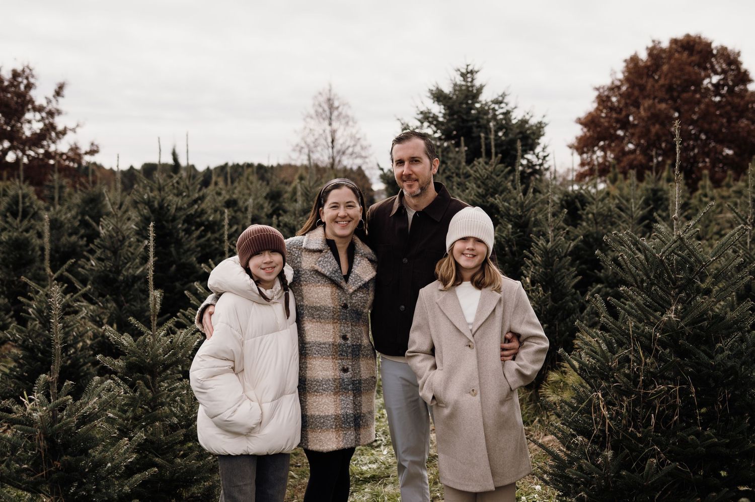 Family of four smiling together among lush green Christmas trees on a tree farm. Lake Elmo, Minnesota.