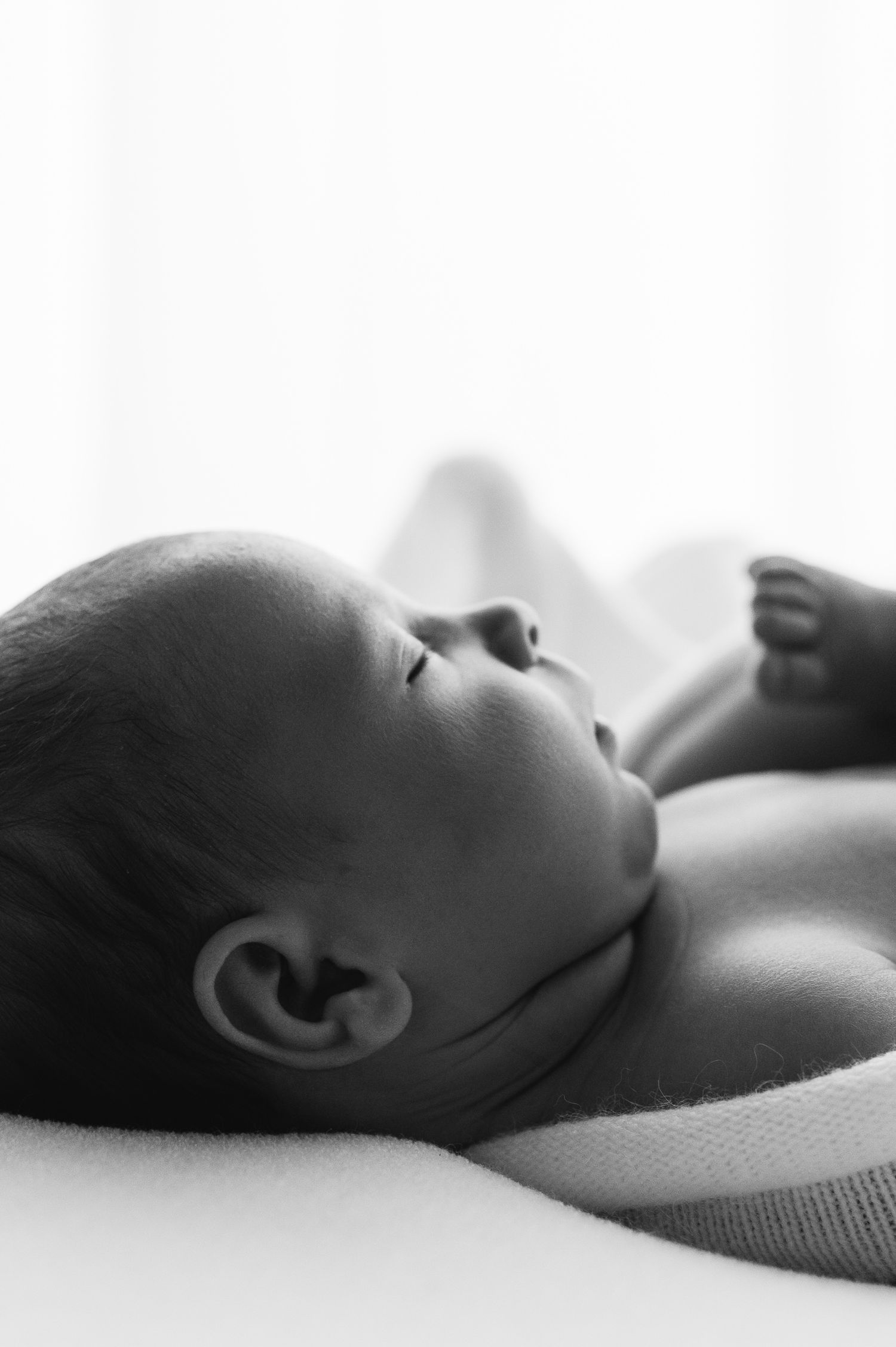 Black and white close-up of peaceful newborn baby lying on soft blanket.