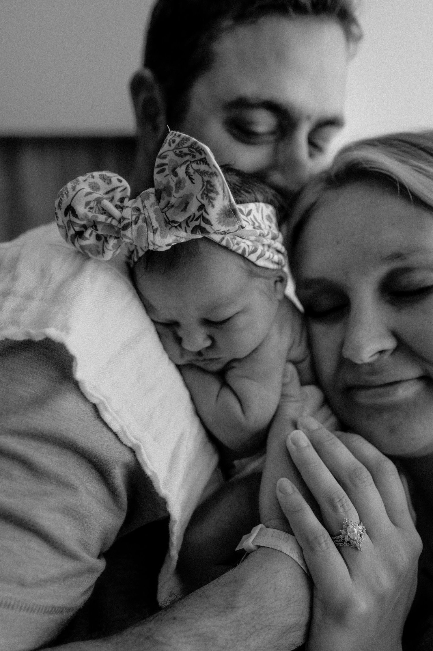 Black and white photo of parents tenderly holding their newborn baby with floral headband. Fresh 48 hospital photos.