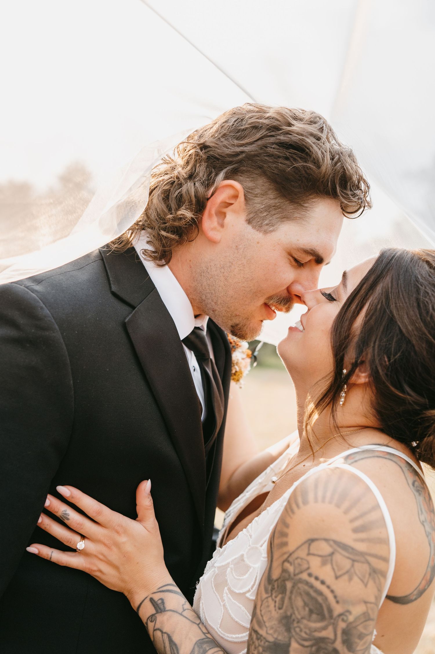 Tattooed bride and groom sharing intimate moment under veil on wedding day. Wisconsin. Minnesota.