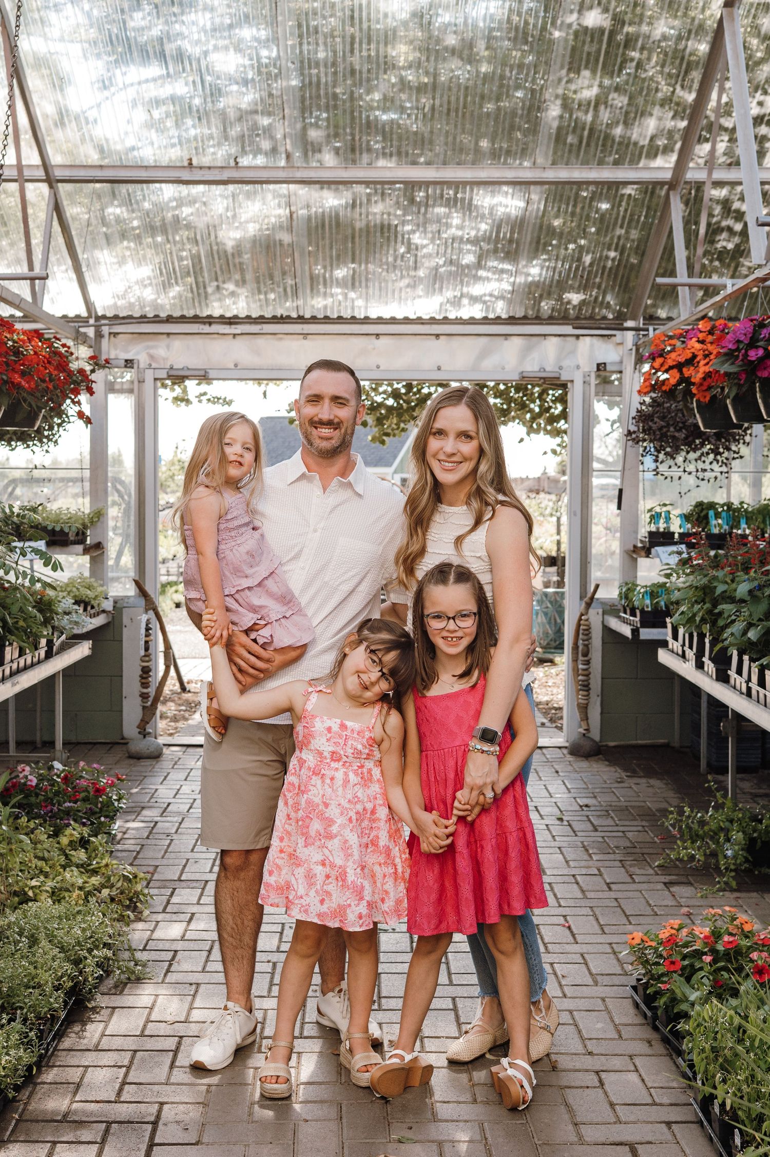 Happy family of five posing together inside a flower-filled greenhouse with brick pathway.