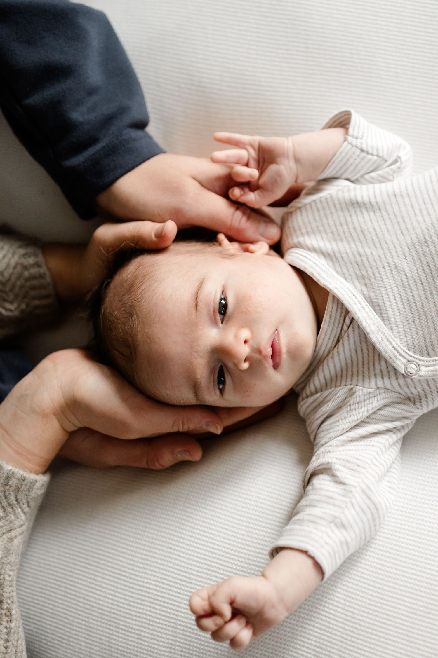 Close-up of a peaceful newborn baby in striped onesie cradled gently in parents hands.