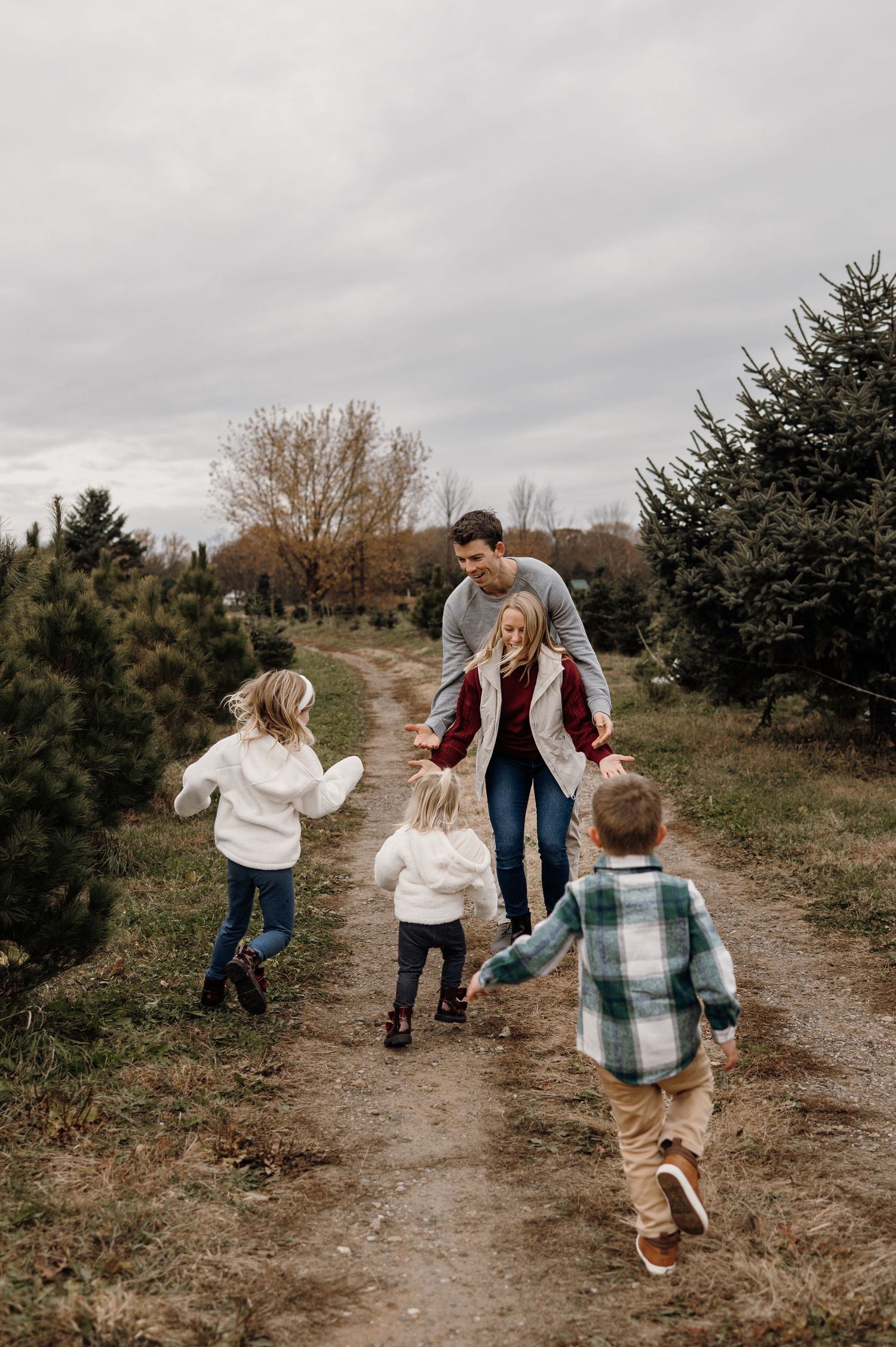 Happy family with three children running toward parents on a Christmas tree farm path. Lake Elmo, Minnesota.