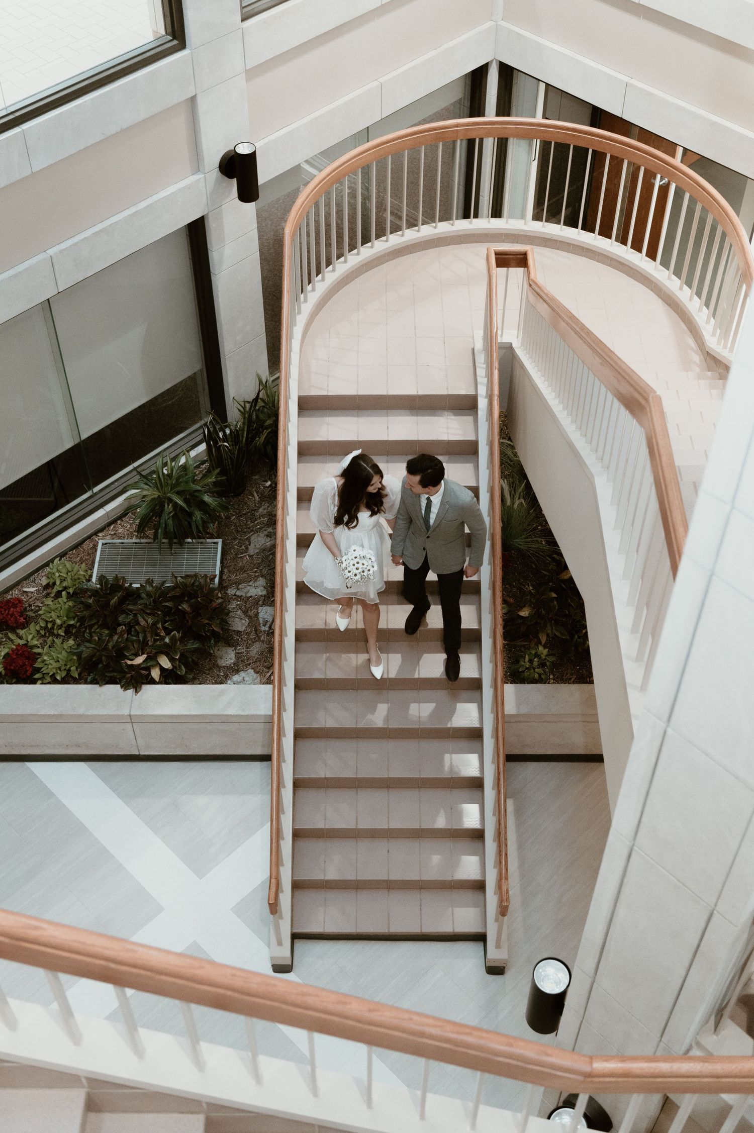 Couple holding hands on curved staircase in bright modern building interior.