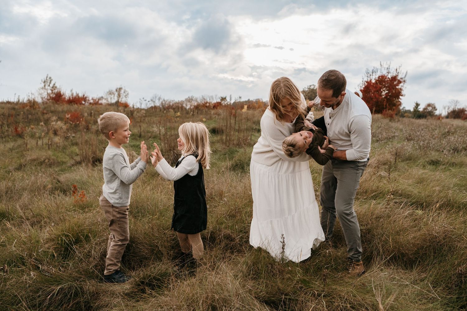 A young family of five shares a joyful candid moment together in an open fall meadow. Woodbury, Minnesota.