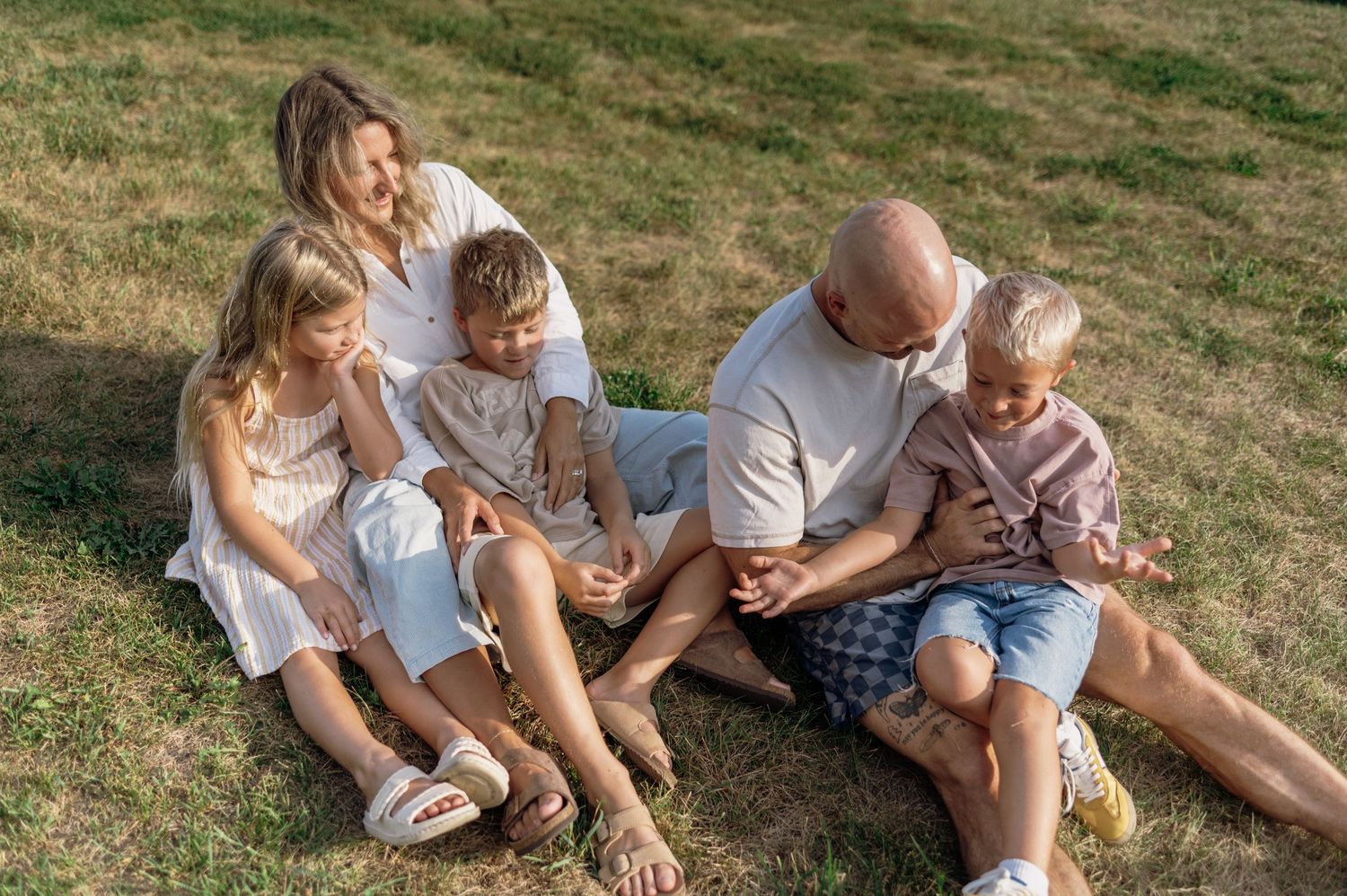 Happy family of five sitting together on green grass in casual summer outfits. Wisconsin. Minnesota.