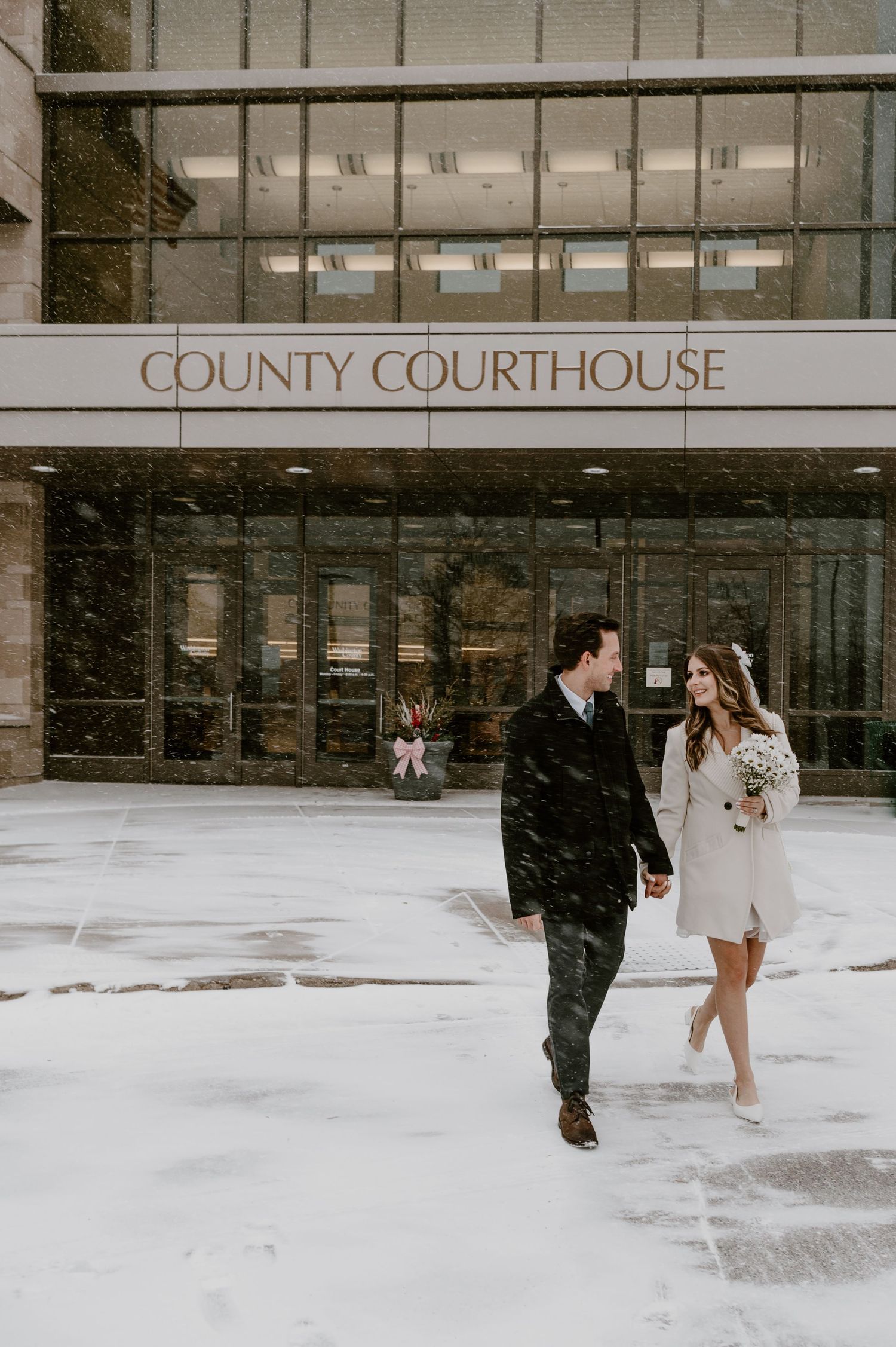 Couple walking hand in hand outside County Courthouse in snowy winter elopement.