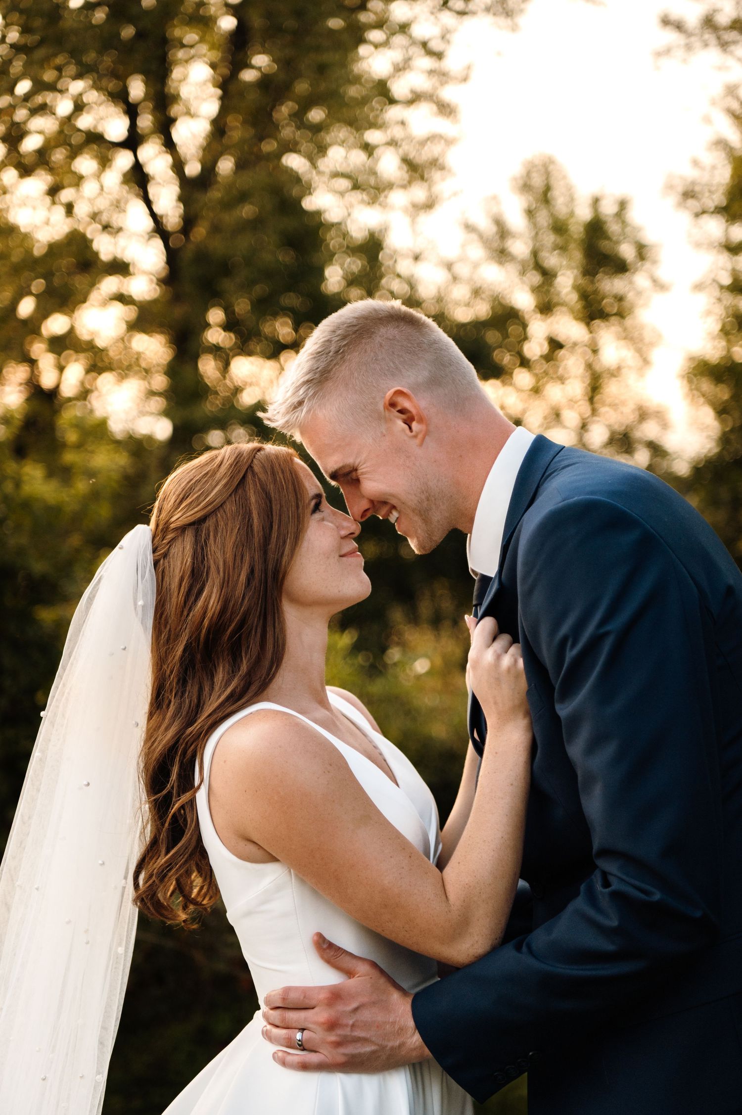 Bride and groom touching foreheads romantically at golden hour outdoor wedding.