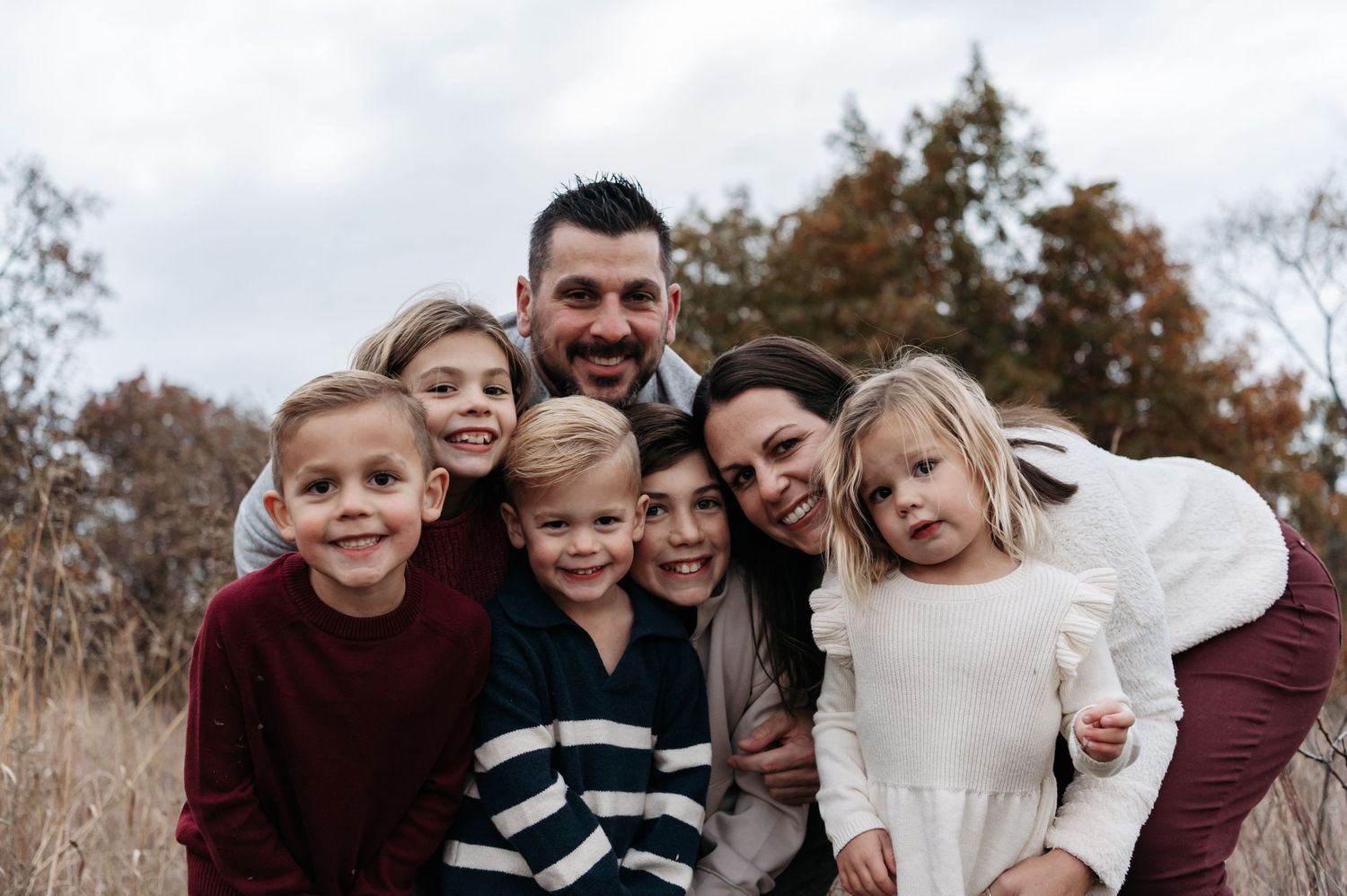 Happy family of seven with five children smiles together in an autumn field portrait. Stillwater, Minnesota.
