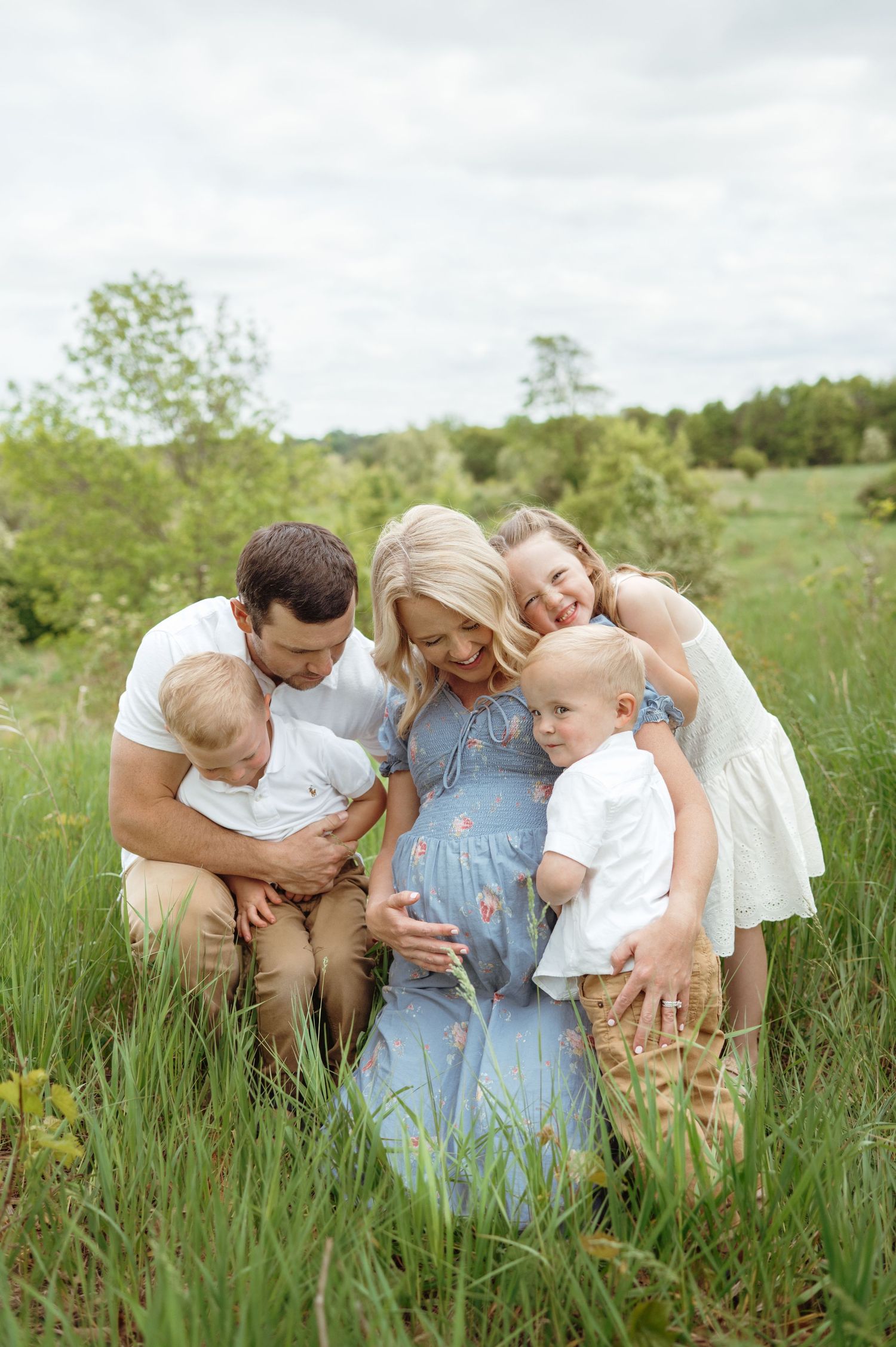 Pregnant mother surrounded by loving family in green meadow, all touching her baby bump.