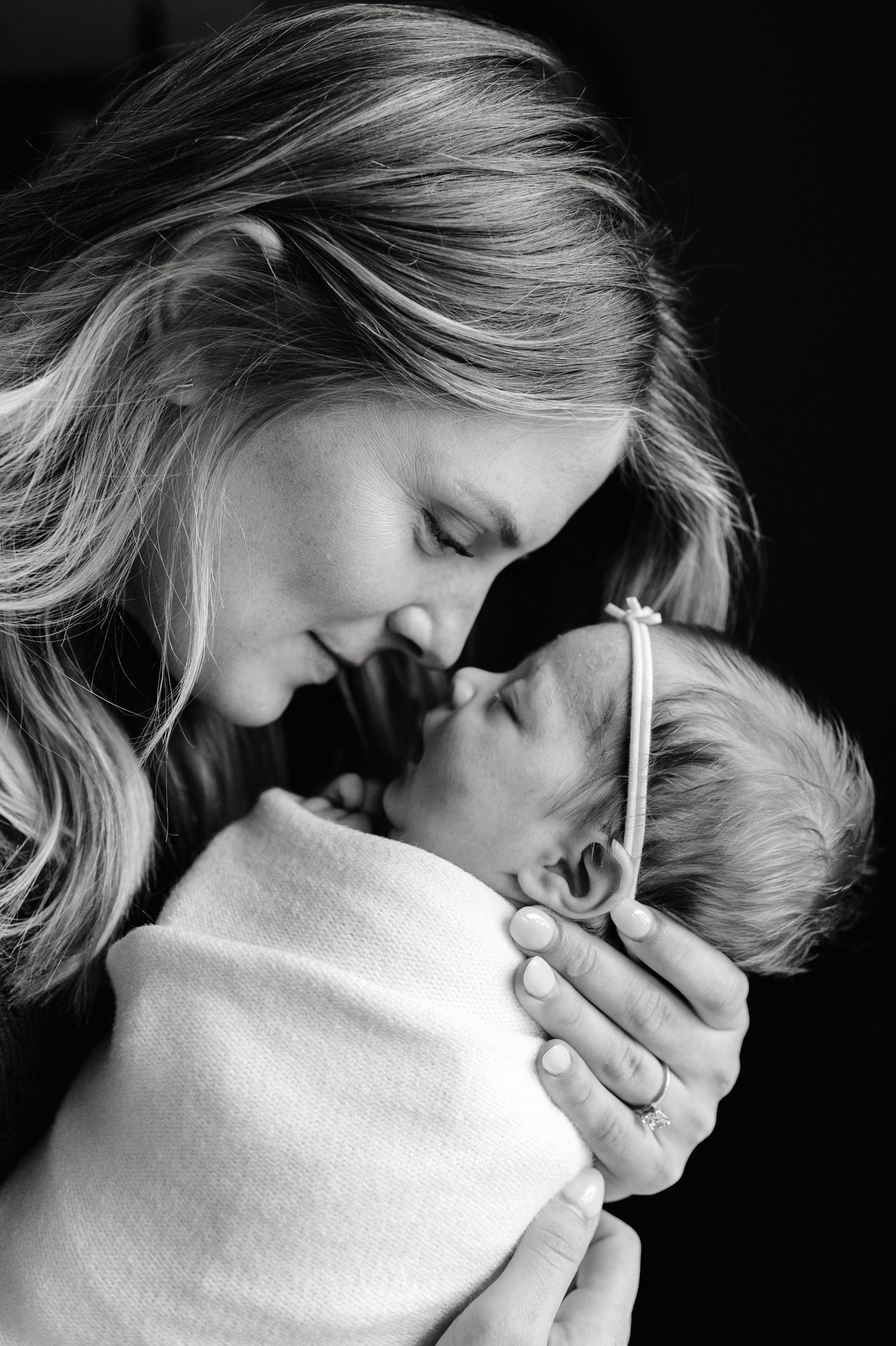 Black and white portrait of a mother tenderly holding her swaddled newborn baby close.