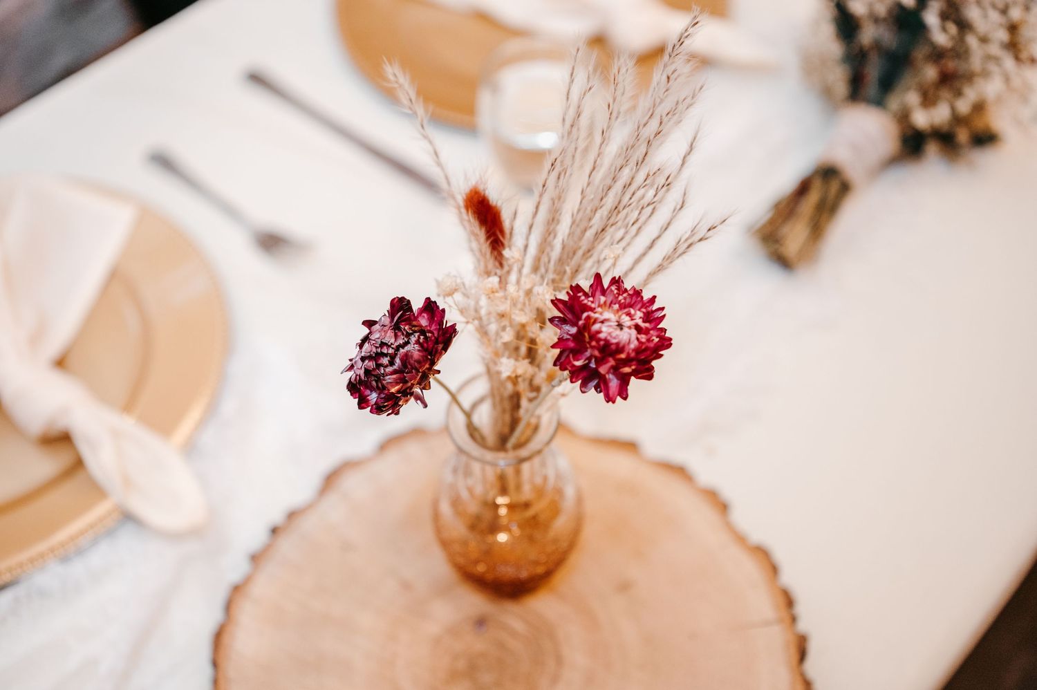 Dried burgundy flowers in amber vase on wood slice wedding table centerpiece.
