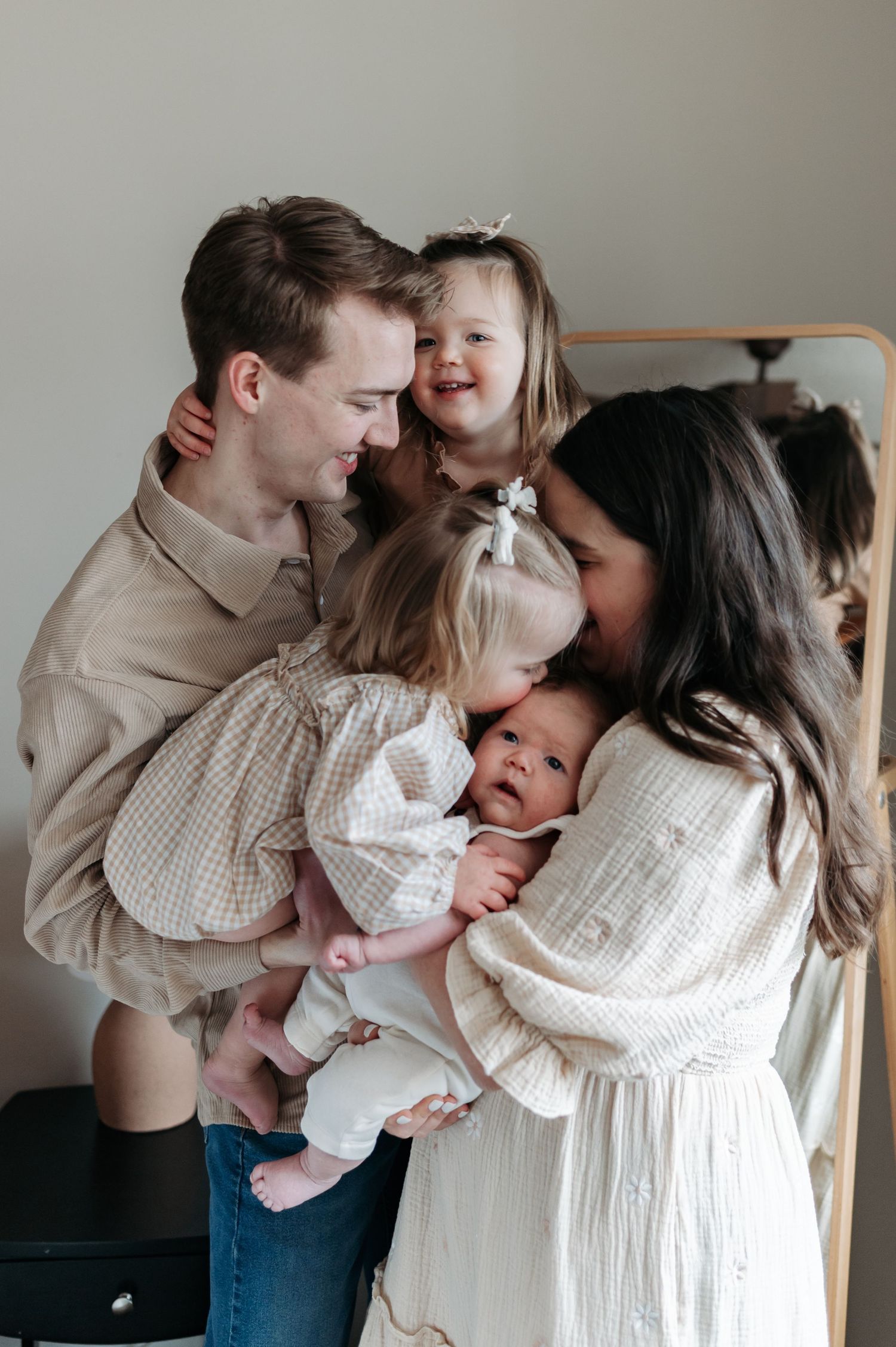 Happy family of four with two toddler girls and newborn baby sharing loving embraces.