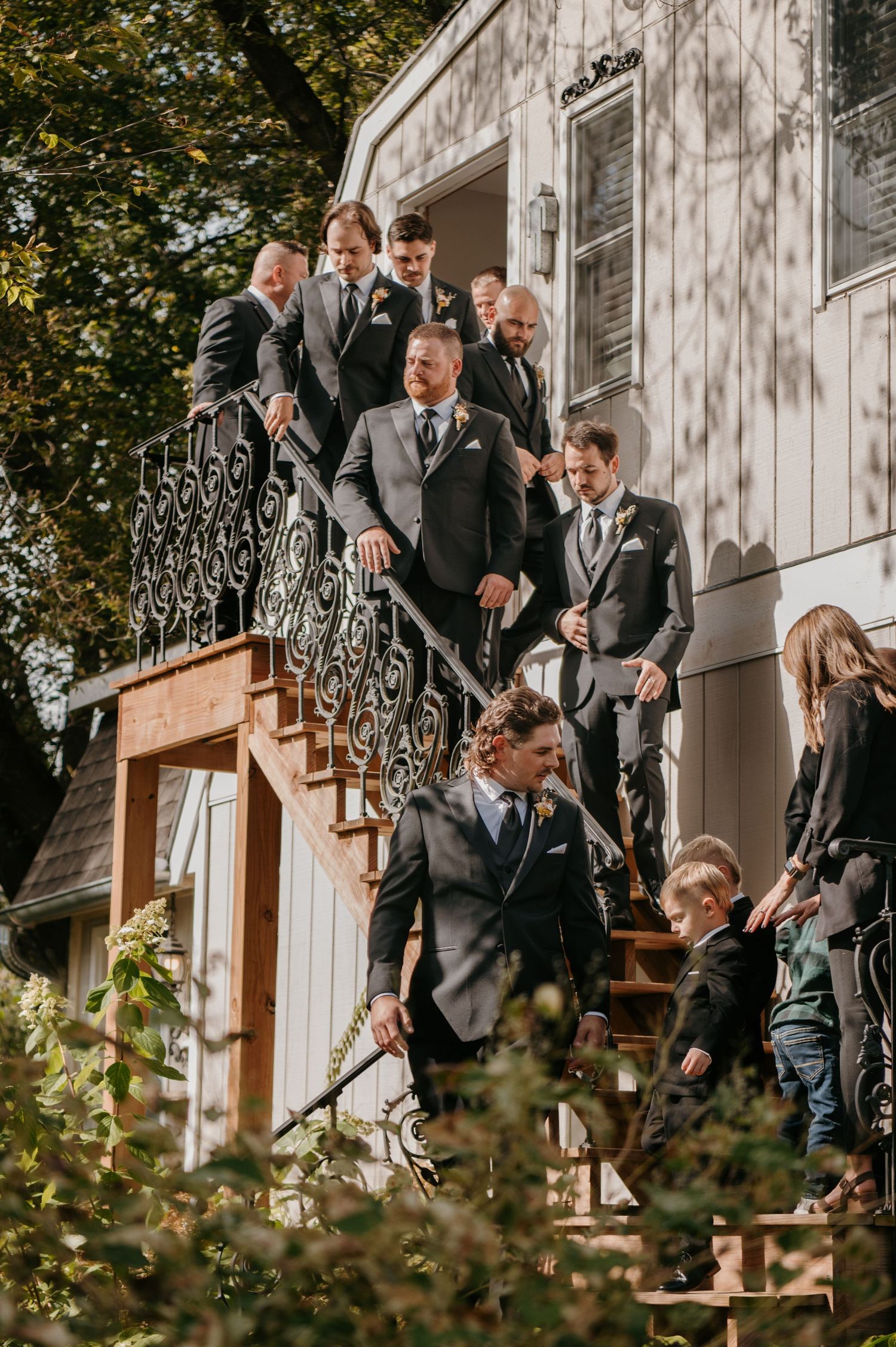 Groomsmen in grey suits descending ornate staircase outside white venue building.