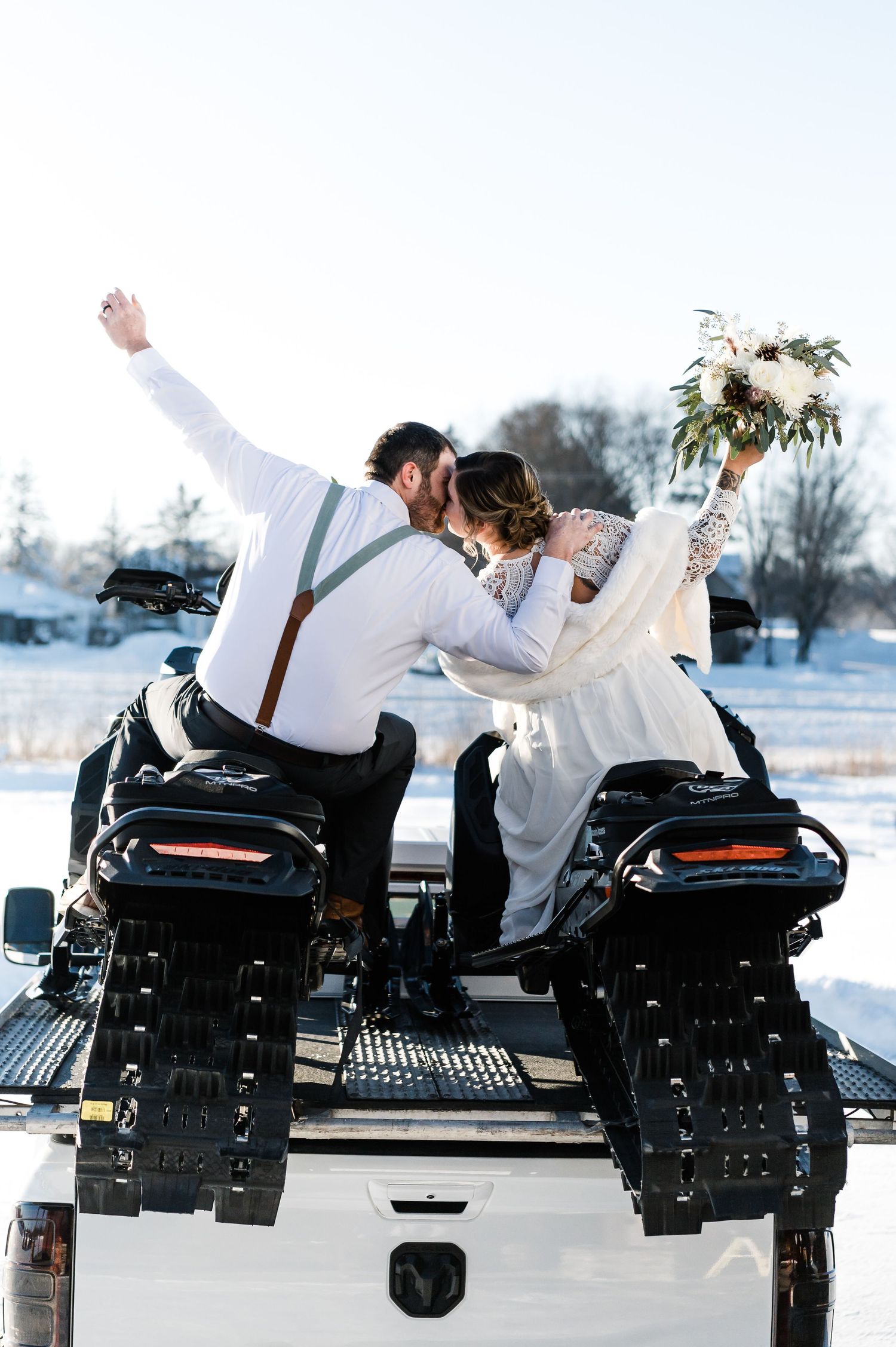 Bride and groom kissing on snowmobiles in snowy winter wedding celebration.