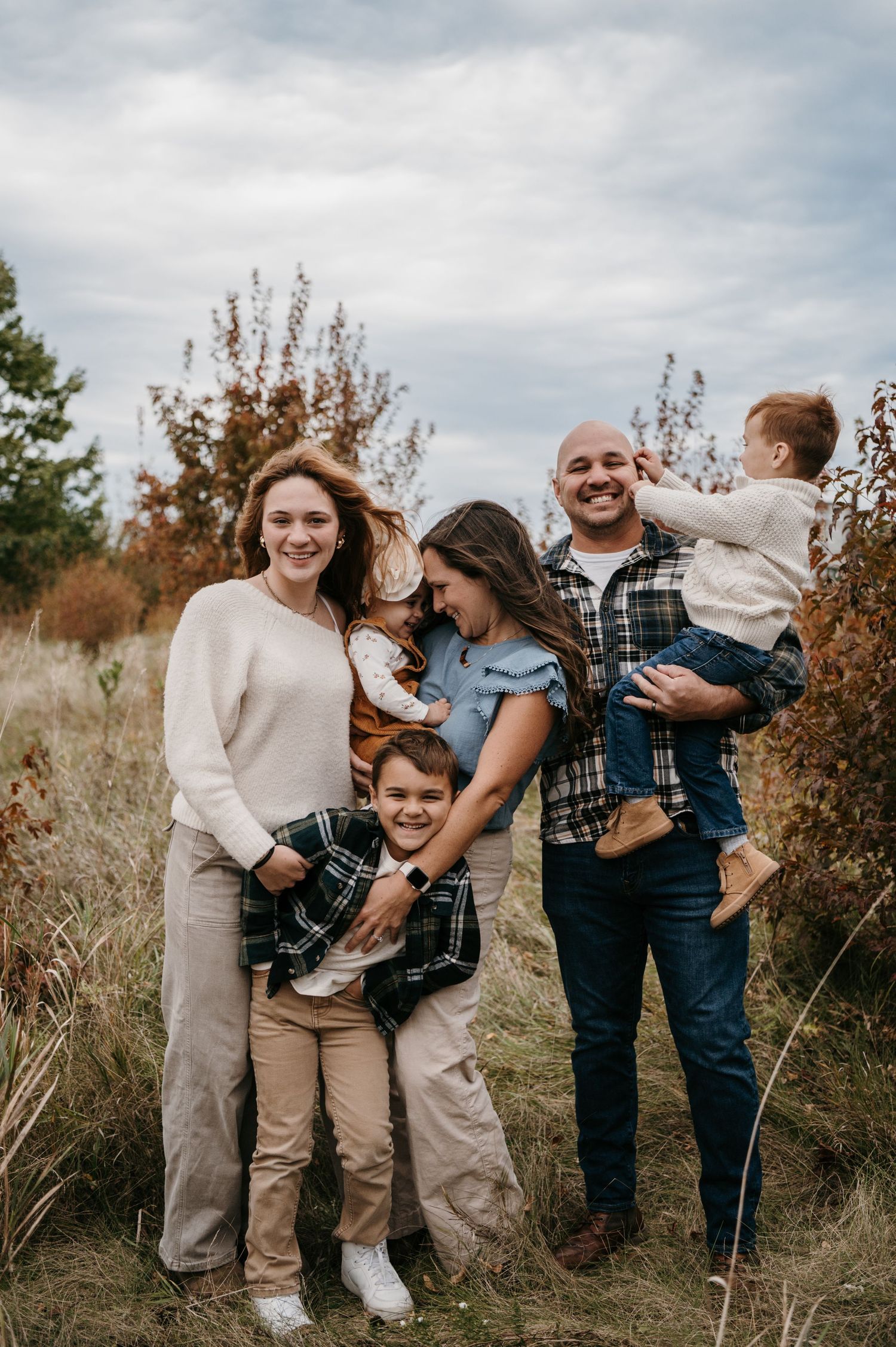A blended family of five smiles together in an autumn field with colorful foliage behind them. Woodbury, Minnesota.