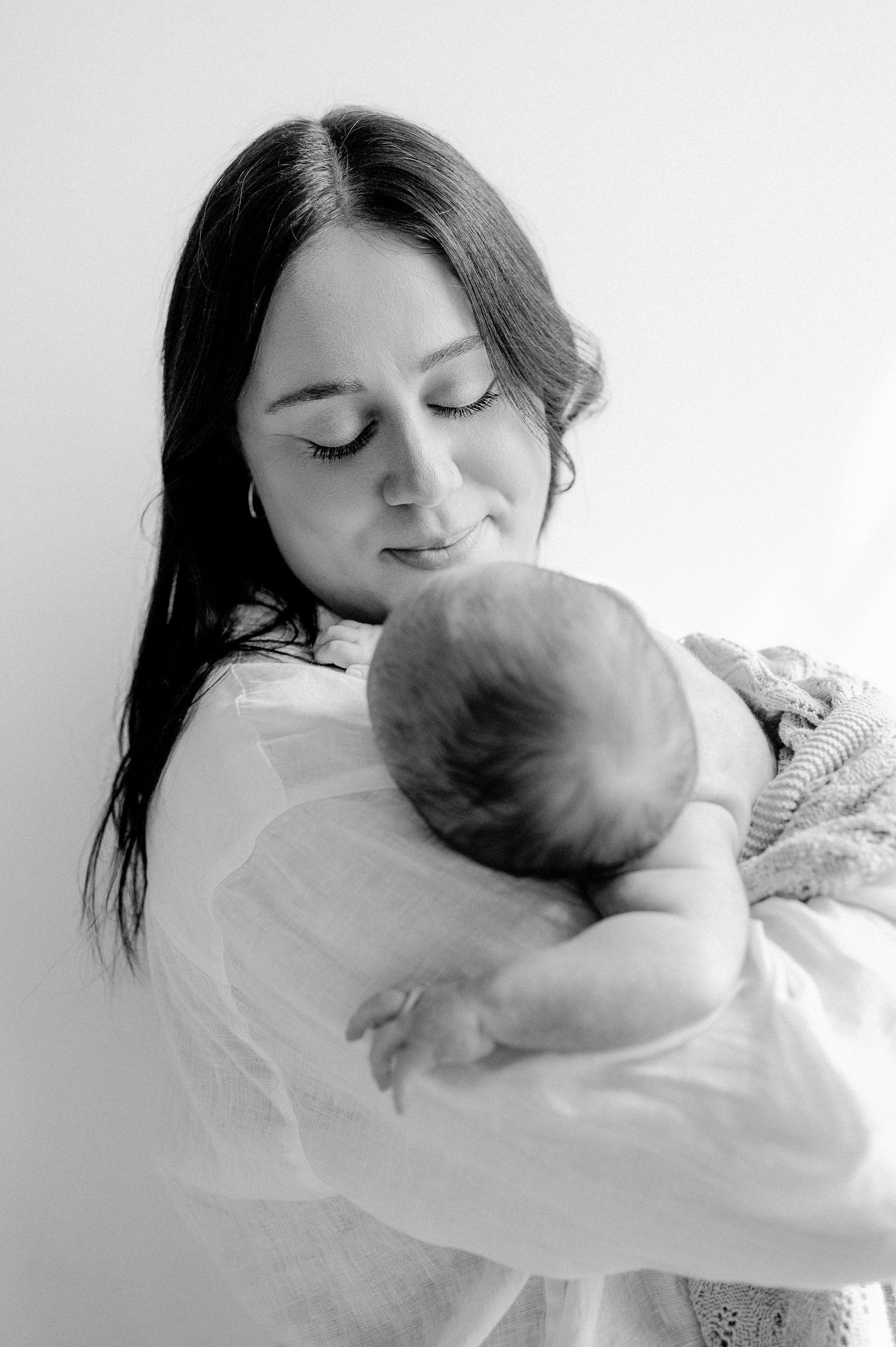 Black and white portrait of dark-haired mother gently cradling her sleeping newborn baby.