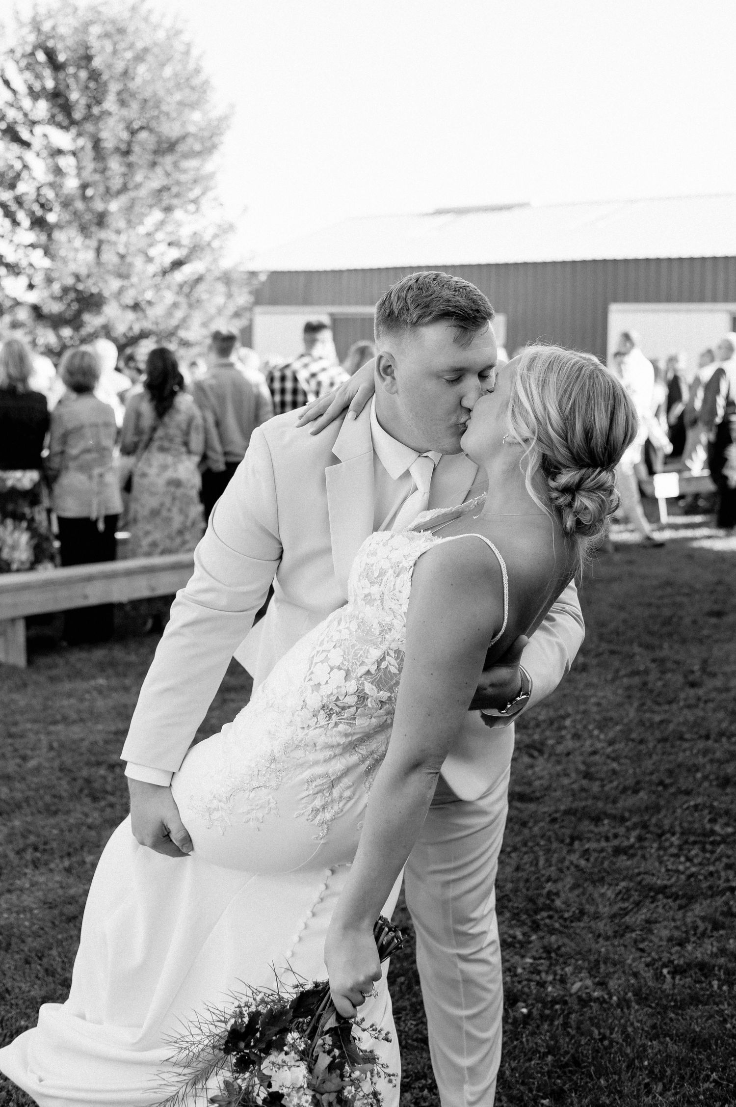 Black and white photo of groom dipping bride for kiss after outdoor barn wedding ceremony.