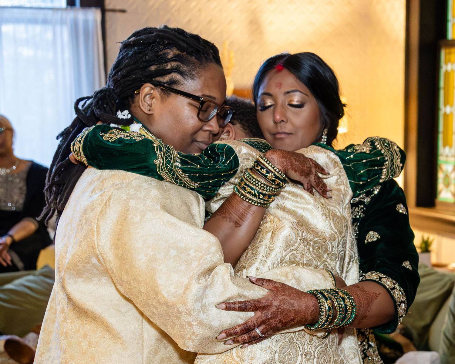 Two people in embroidered ivory and green wedding attire share a heartfelt embrace during a South Asian wedding ceremony.