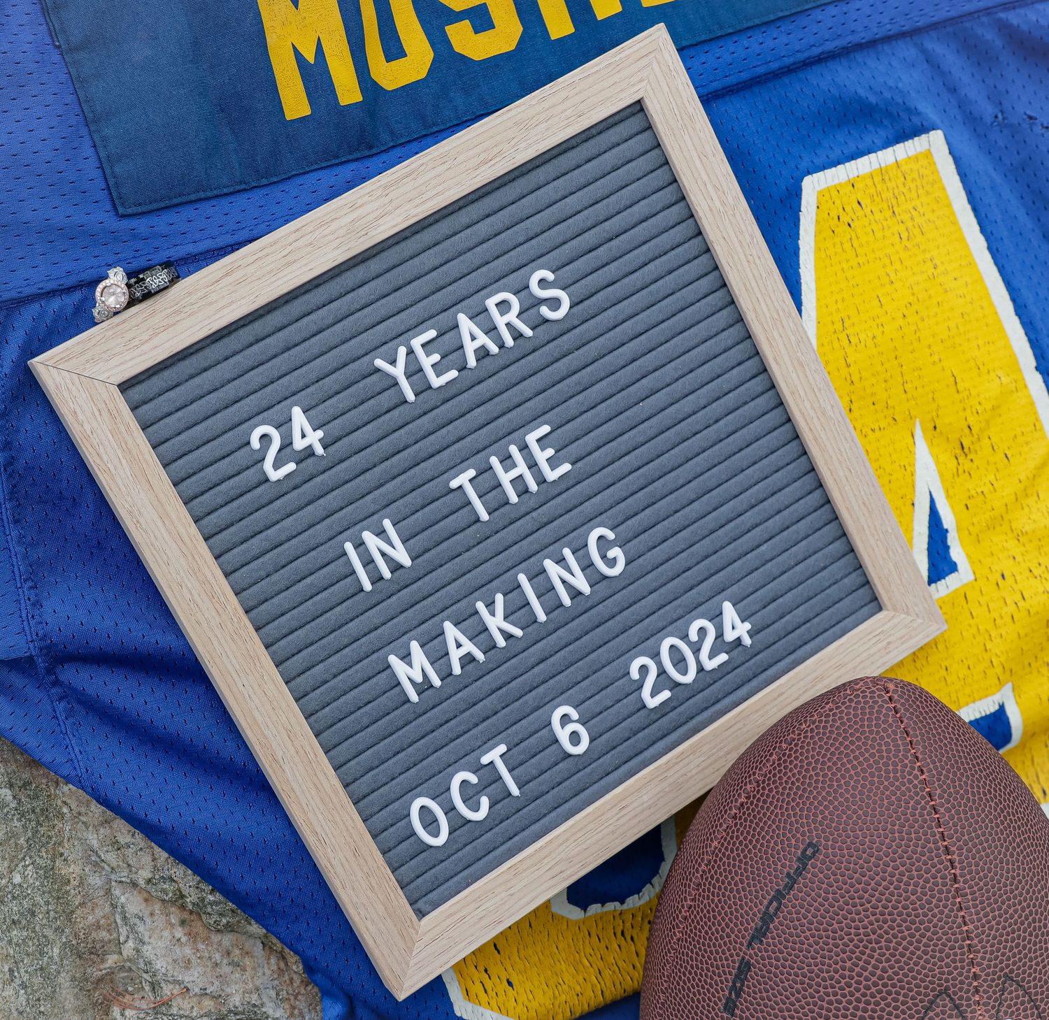 A letter board reading 24 years in the making Oct 6 2024 rests on a blue football jersey beside a football.