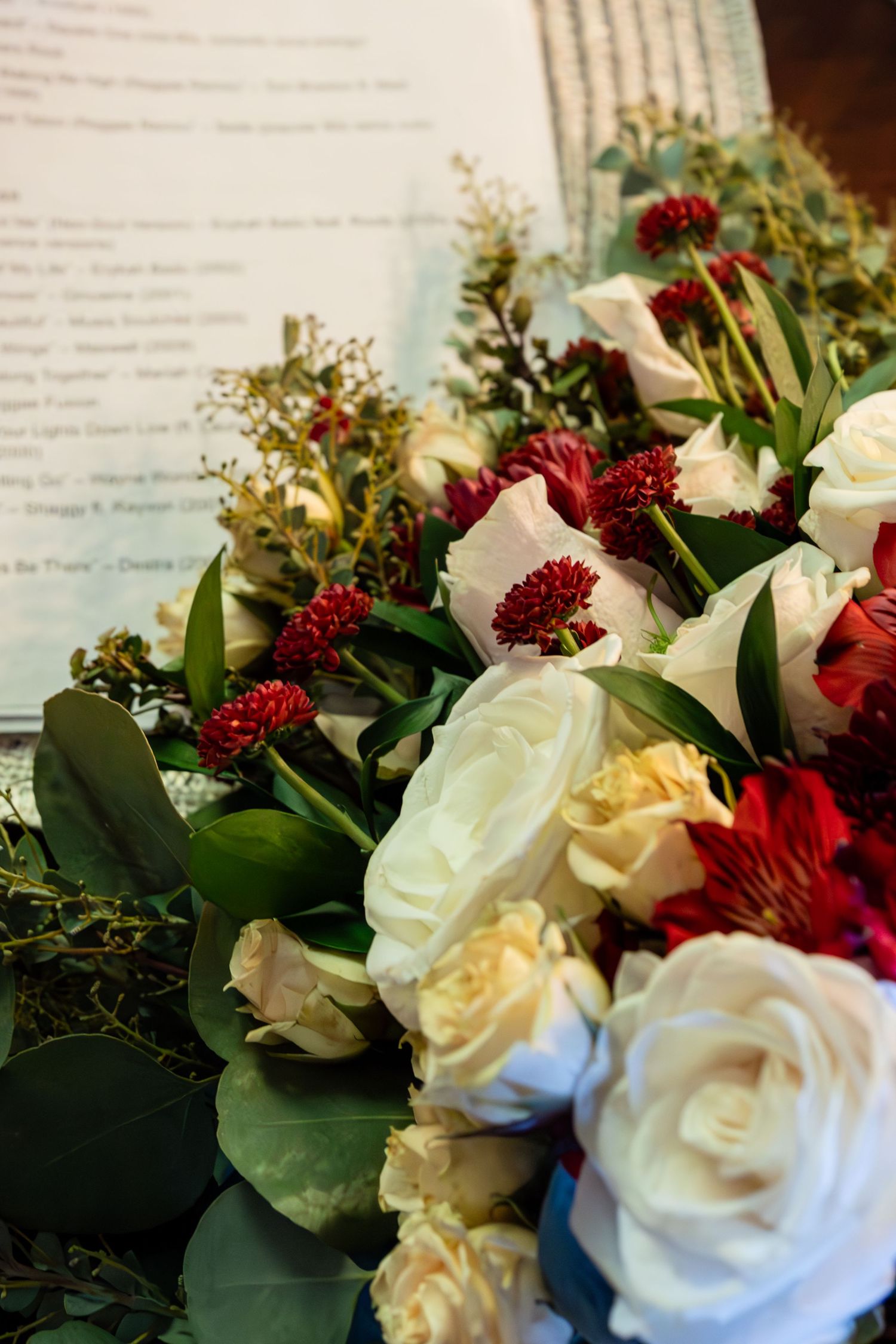 Bridal bouquet of cream roses, red flowers, and leafy greens placed next to a printed ceremony program.