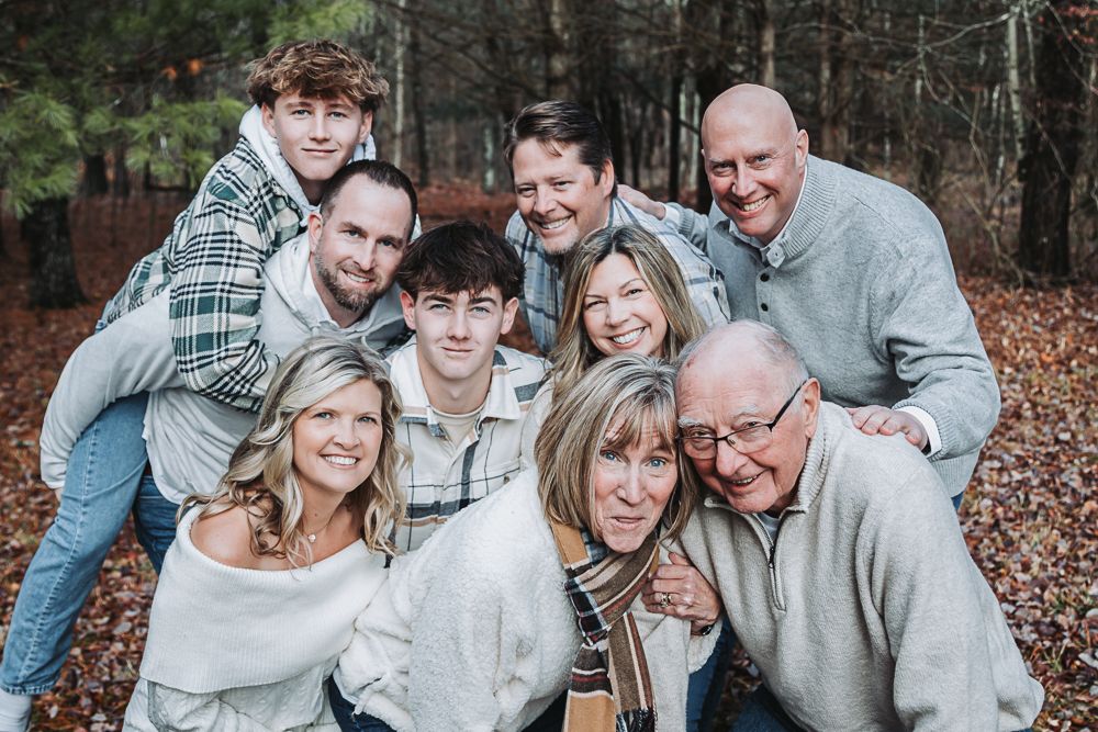 Smiling multigenerational family huddles close together for a portrait in an autumn forest.
