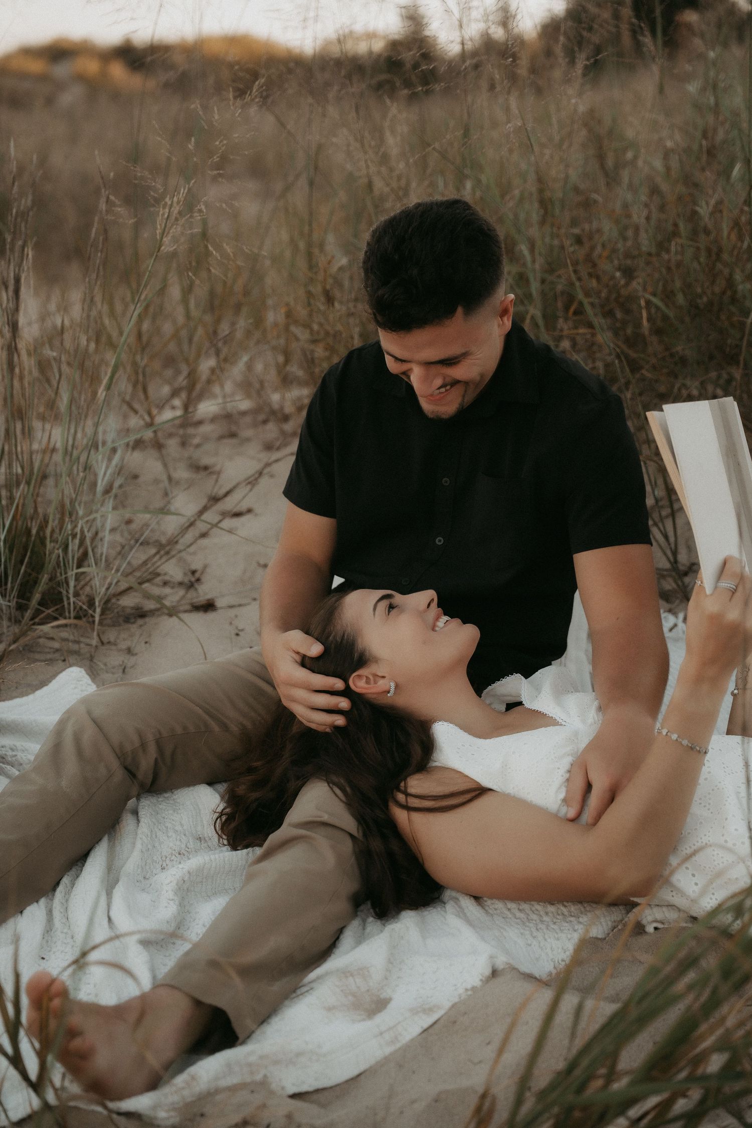 Intimate outdoor couple photoshoot showing tender moments on a white blanket in a natural setting.