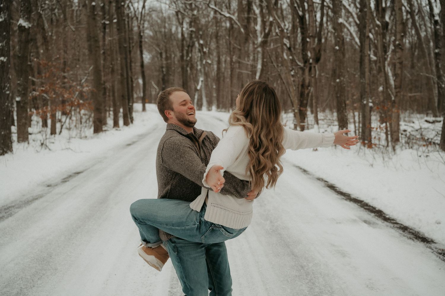 A couple embraces while walking along a snow-covered forest path during winter.