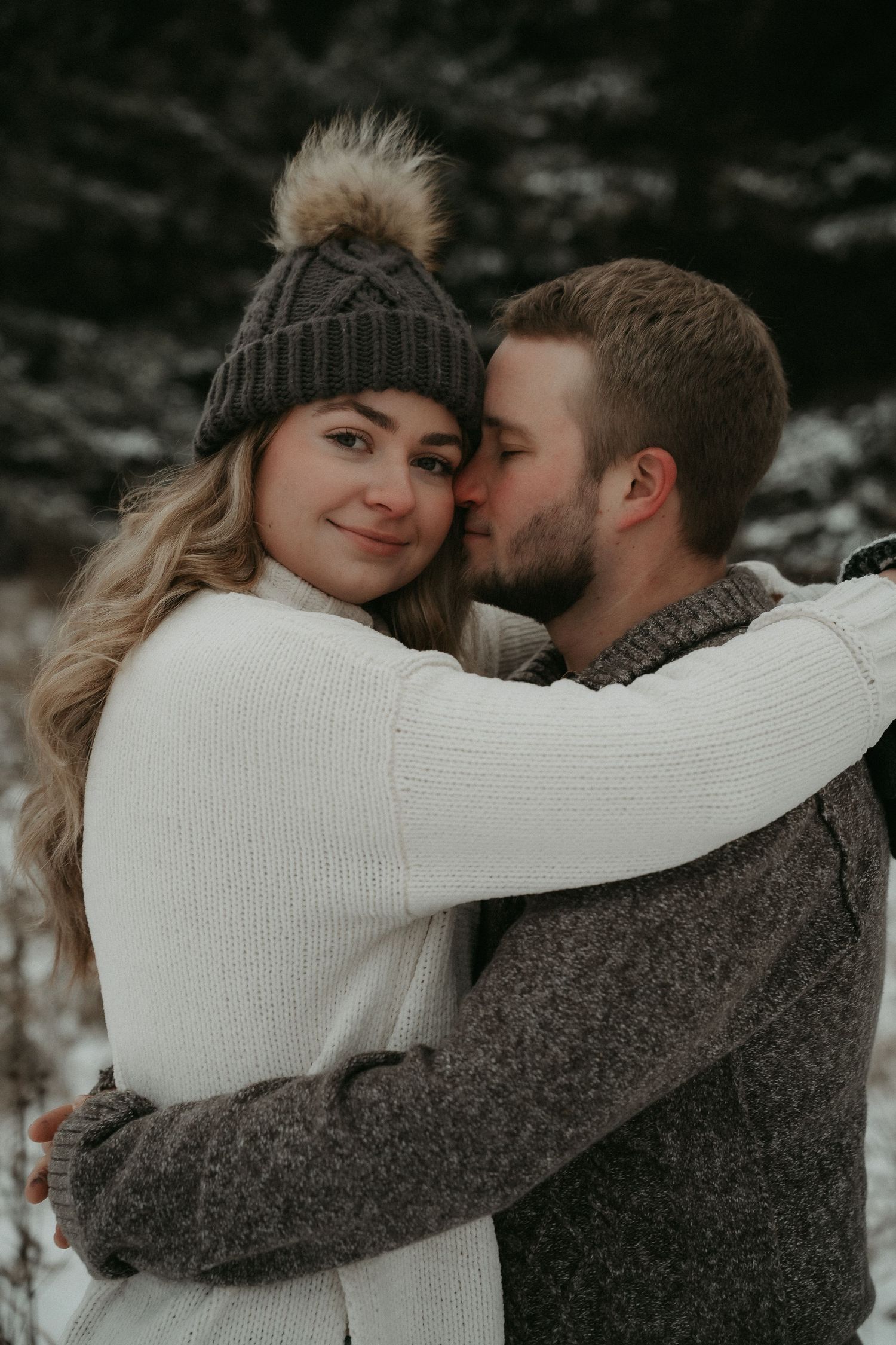 A romantic winter portrait of a couple embracing outdoors, wearing cozy sweaters and a knit beanie.