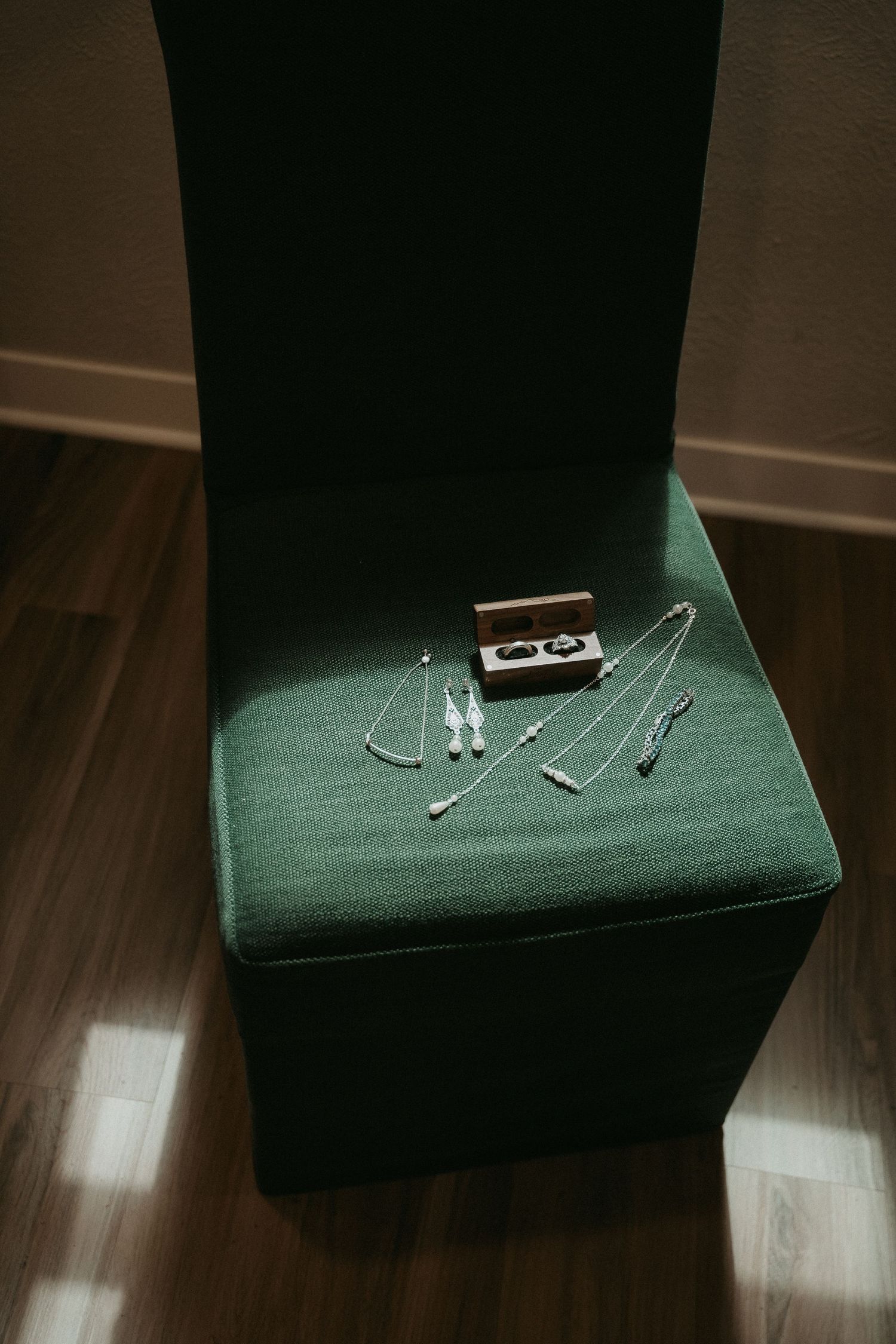 A green upholstered chair arm with a pair of glasses resting on top in low lighting.