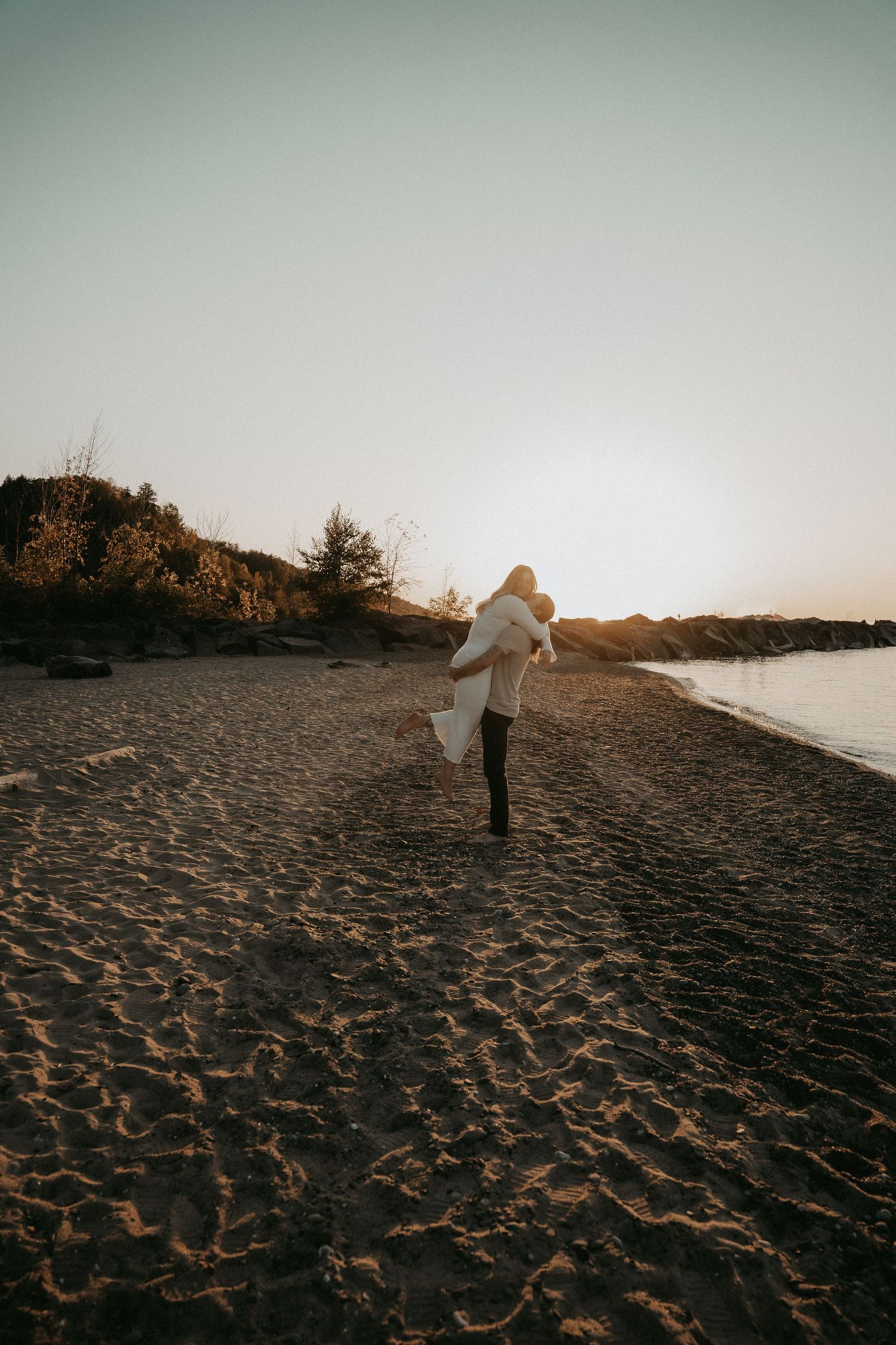 A person in white walks along a sandy beach at sunset, creating a serene coastal silhouette.