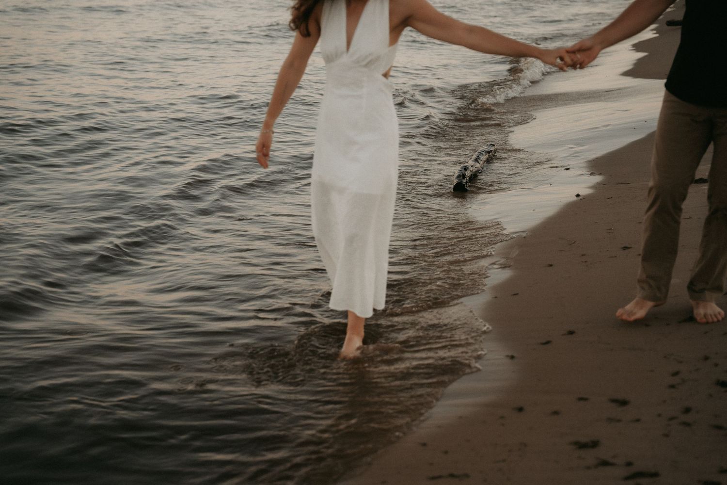 People holding hands while walking barefoot along the shoreline at sunset on a sandy beach.