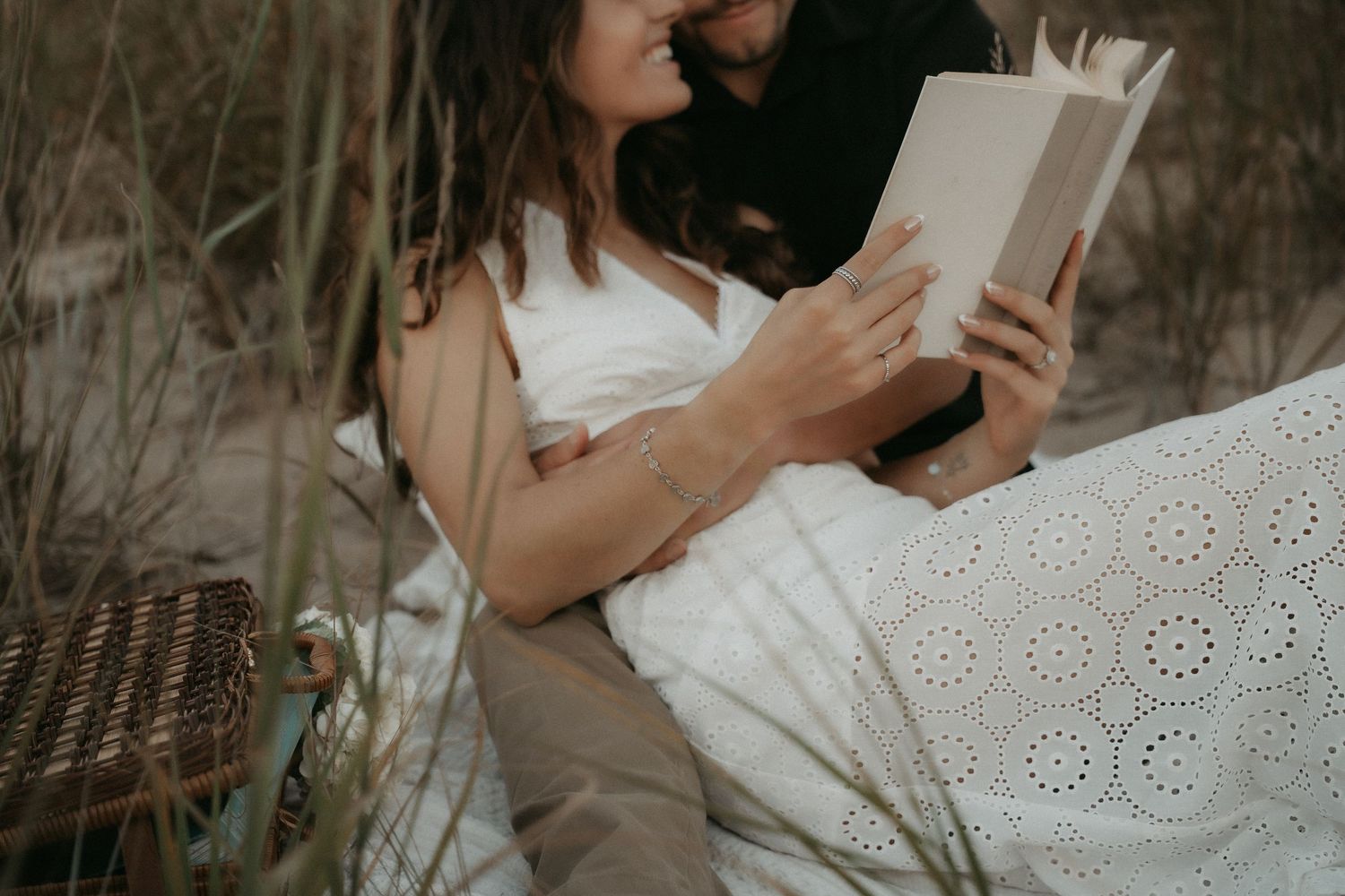 Person in a white dress sits outdoors reading a book against a natural backdrop.