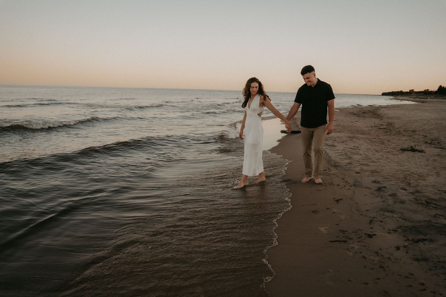 People walking along a misty beach at sunset with waves gently rolling onto the shore.
