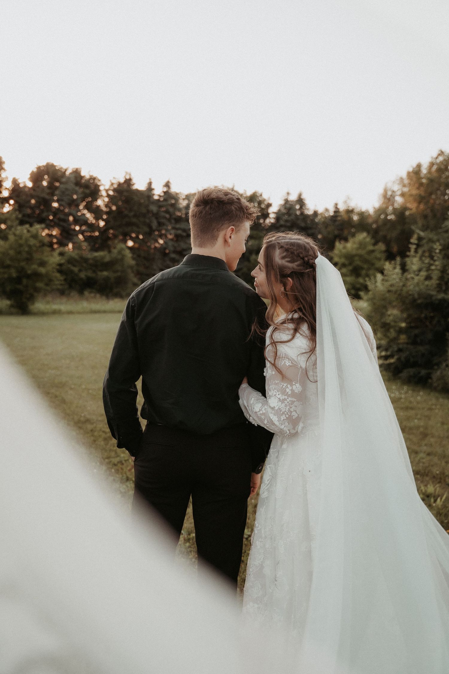 Romantic newlywed couple embracing in a golden sunset with forest backdrop.