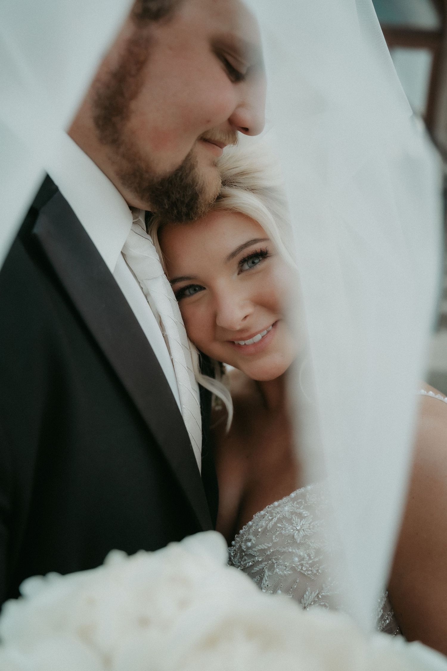 Romantic wedding portrait series showing intimate moments between bride and groom through flowing white veil.