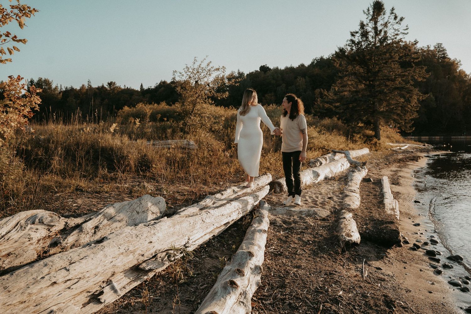 A couple in white outfits walks along a sandy beach path during a sunset photo session at dusk.