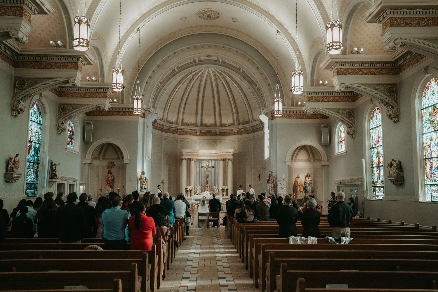 Interior view of a traditional church sanctuary with white vaulted ceilings, wooden pews and stained glass windows.