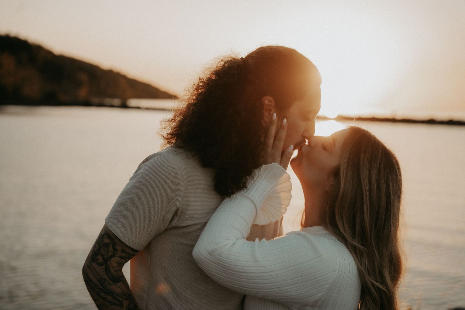 Silhouetted couple embraces tenderly during golden sunset by the water.