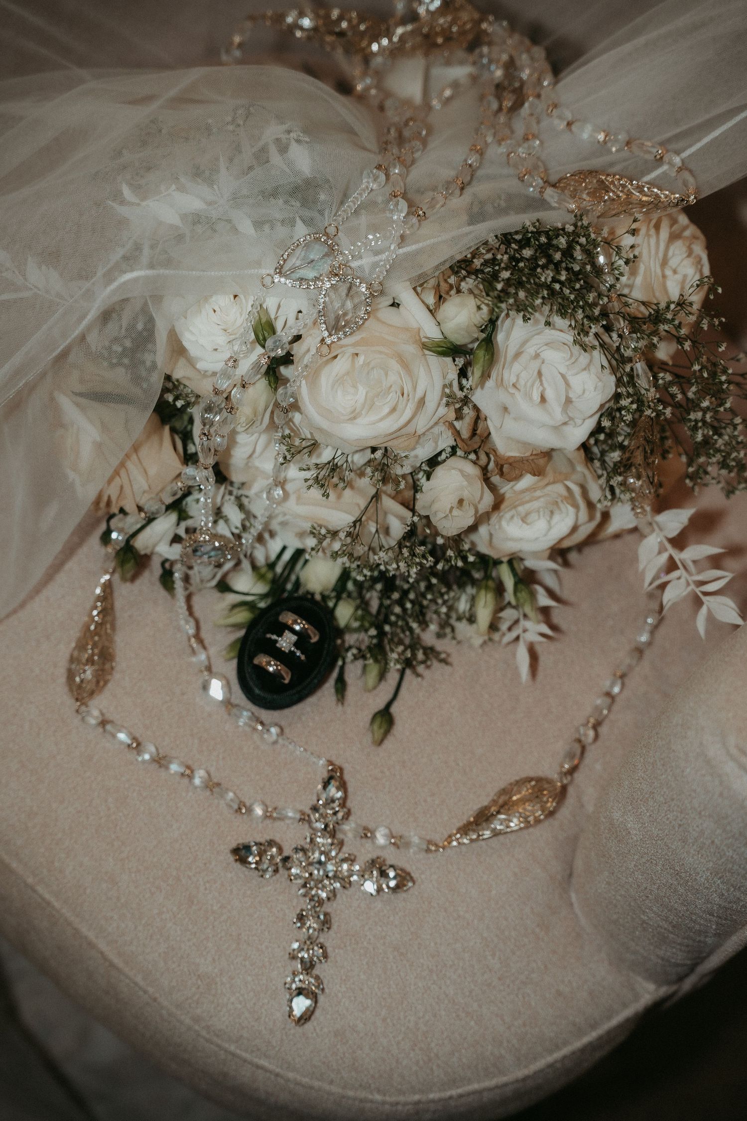 Wedding details featuring white roses, baby's breath bouquet and crystal cross necklace on tulle fabric.