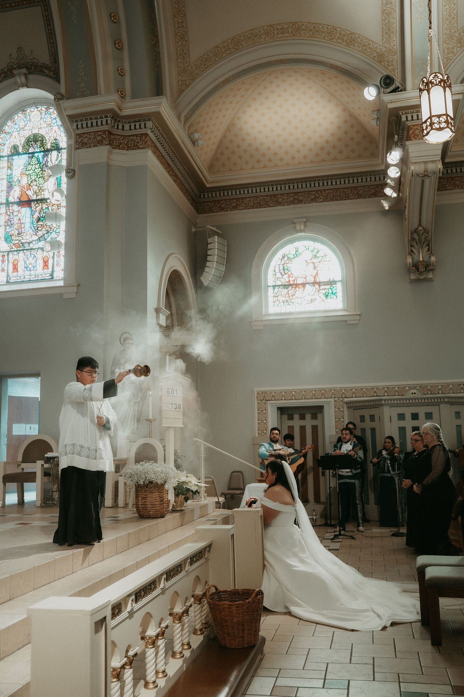 A traditional Catholic wedding ceremony takes place in an ornate church with stained glass windows and incense rising from a censer.