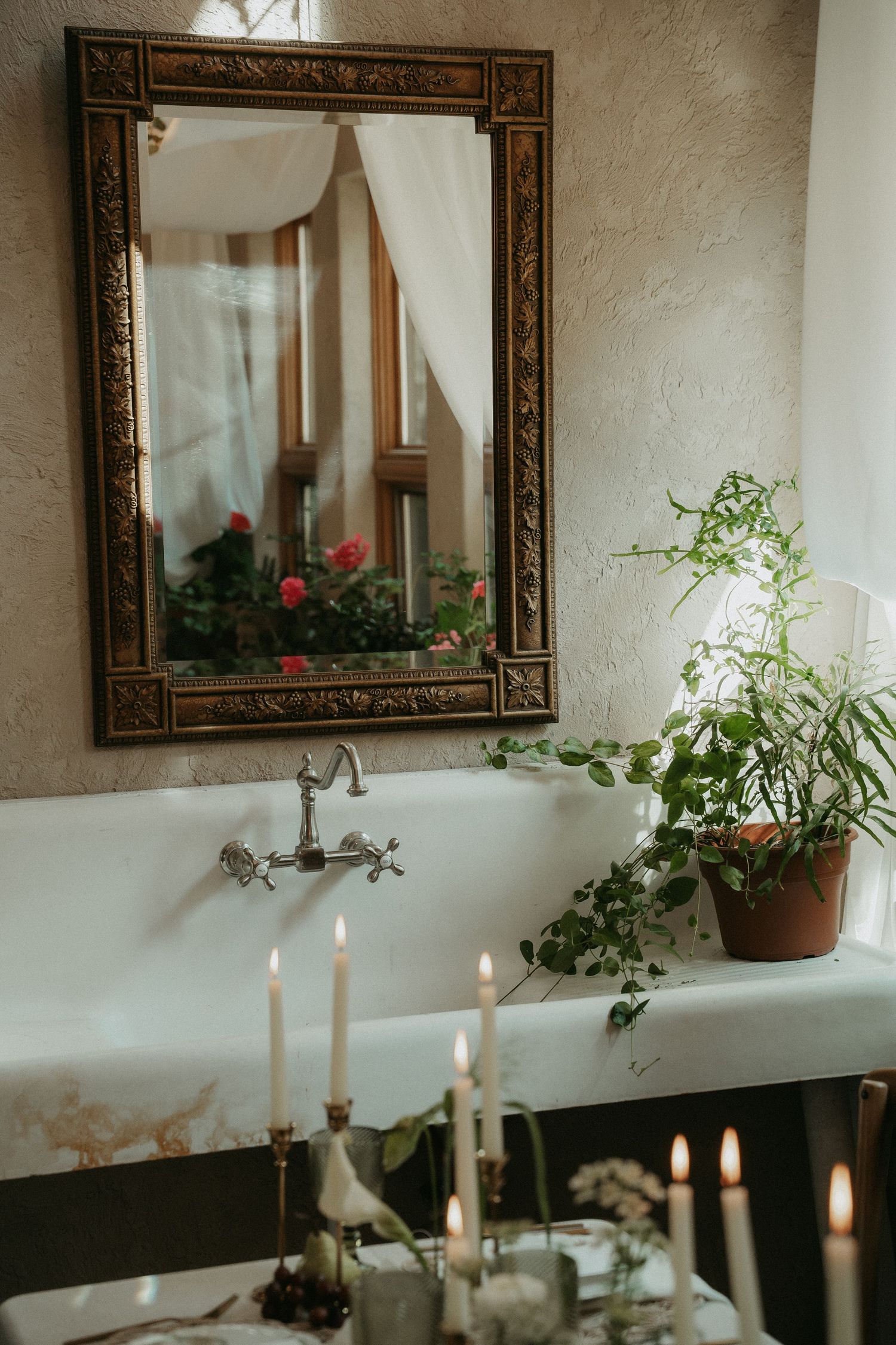Elegant vintage bathroom with ornate mirror, lit candles, green potted plant, and classic clawfoot tub with antique faucet.