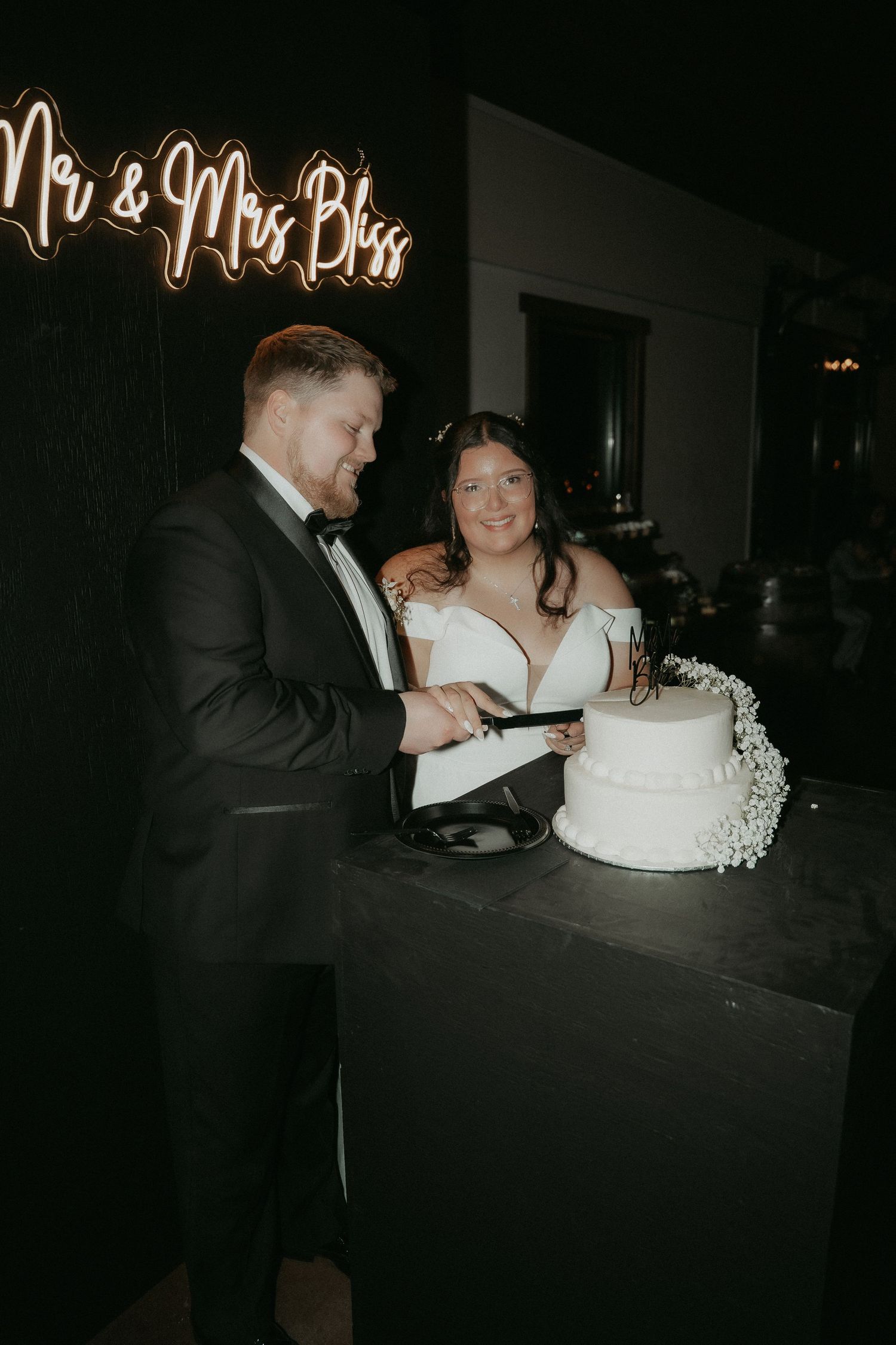 A couple shares a tender moment while cutting their wedding cake together in a dimly lit reception venue.