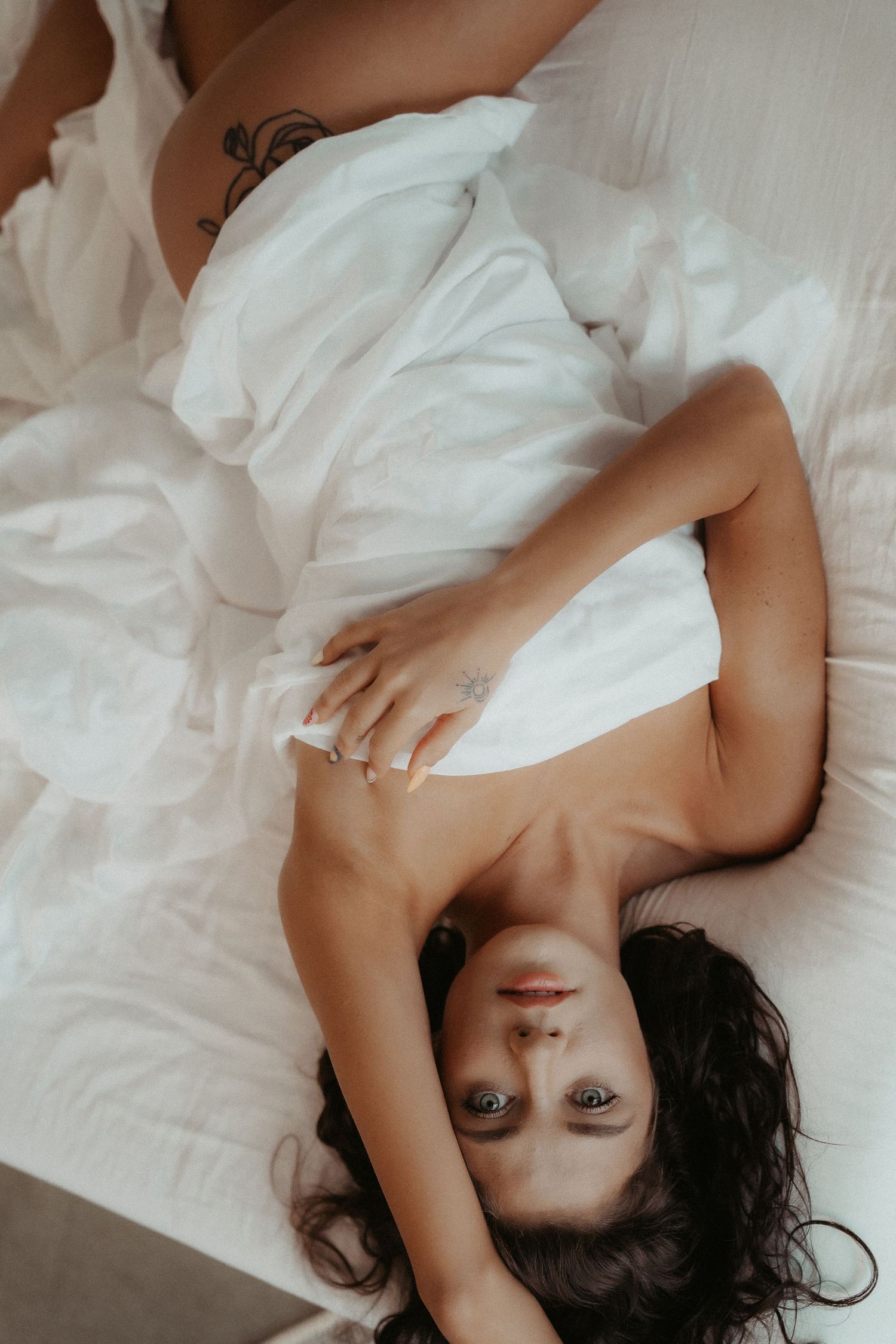 Person with dark hair lying on white bedding in a relaxed pose wearing white clothing.