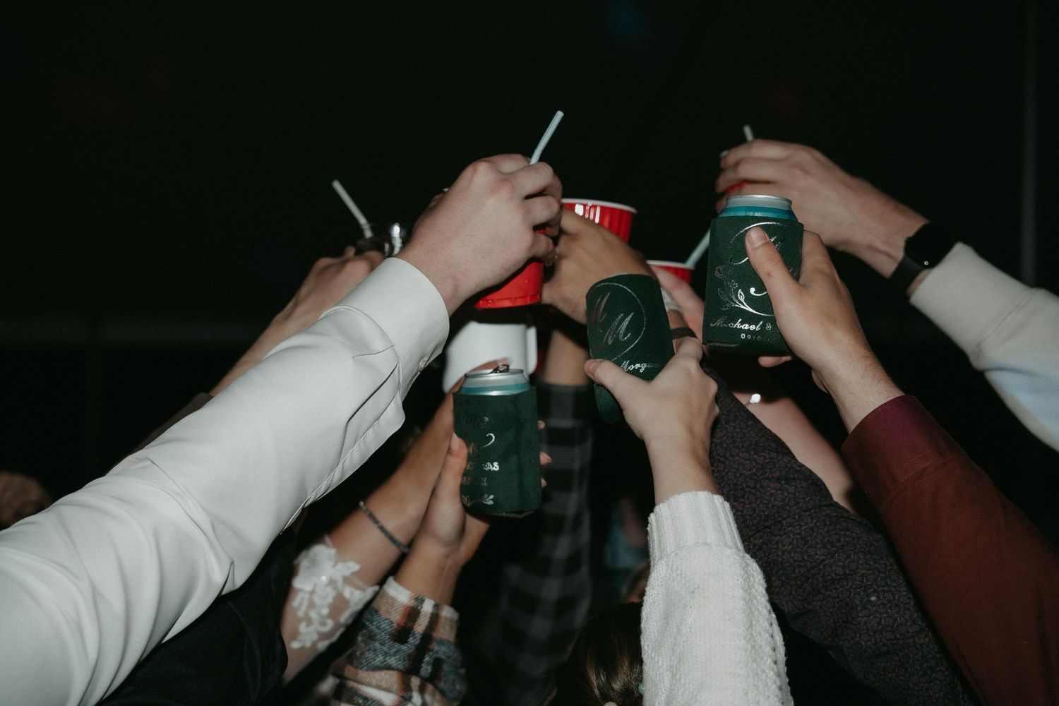 Group of hands raising and clinking glass bottles together in a celebratory toast against dark background.