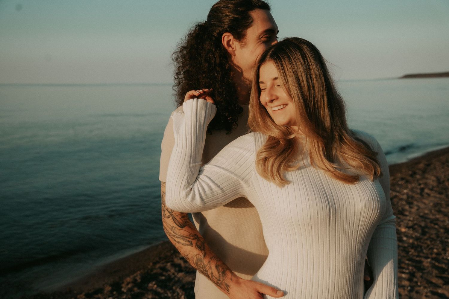 A couple embraces on a rocky beach at sunset, creating a romantic silhouette against the ocean backdrop.