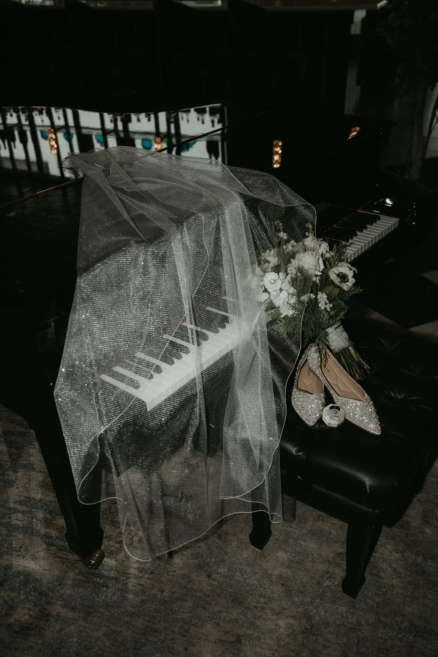 Elegant bridal veil flowing over hardwood floor with wedding shoes visible in dramatic black and white photography.