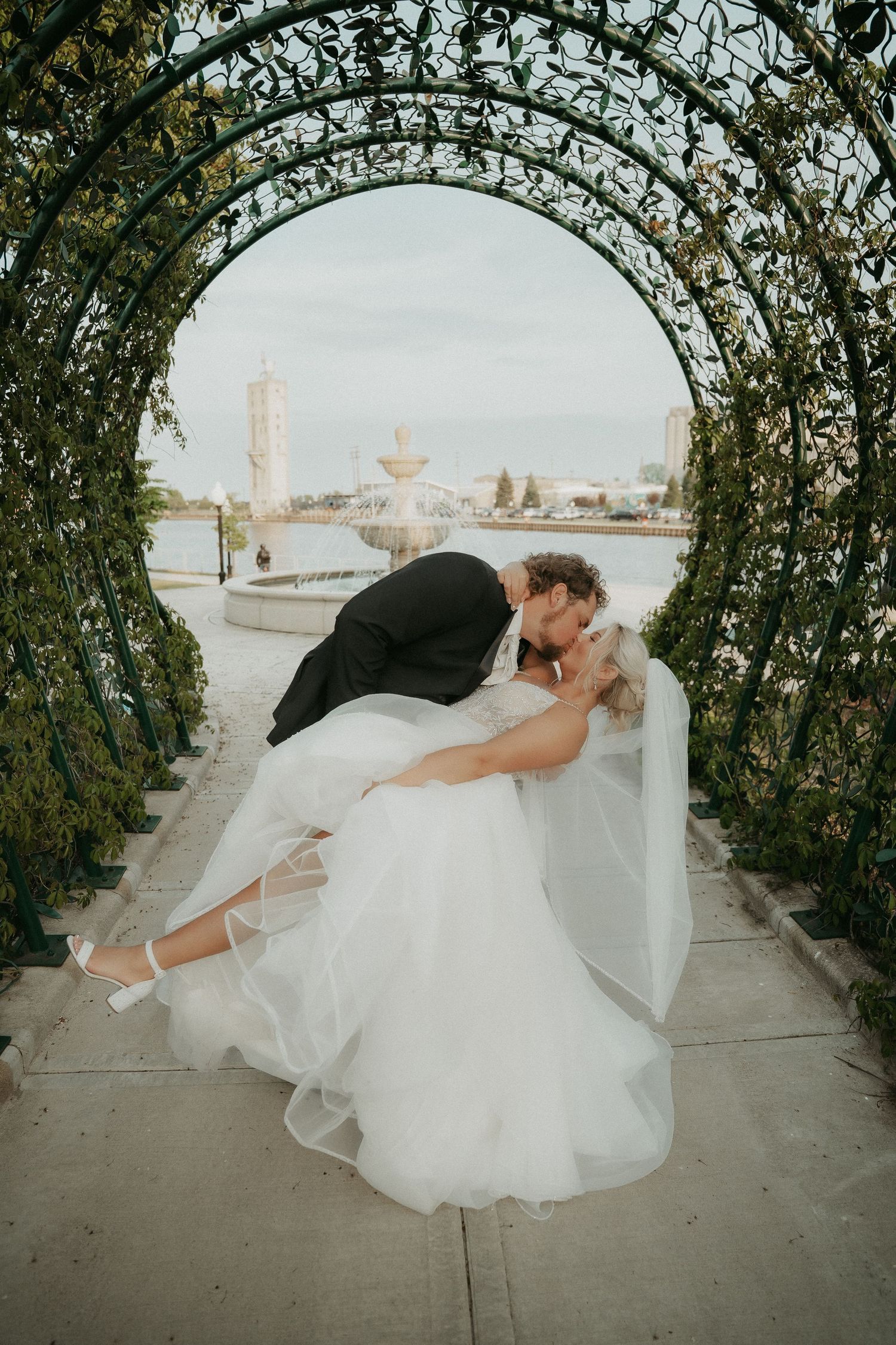 A sequence of dance dip poses under an arched garden walkway covered in climbing vines and greenery.