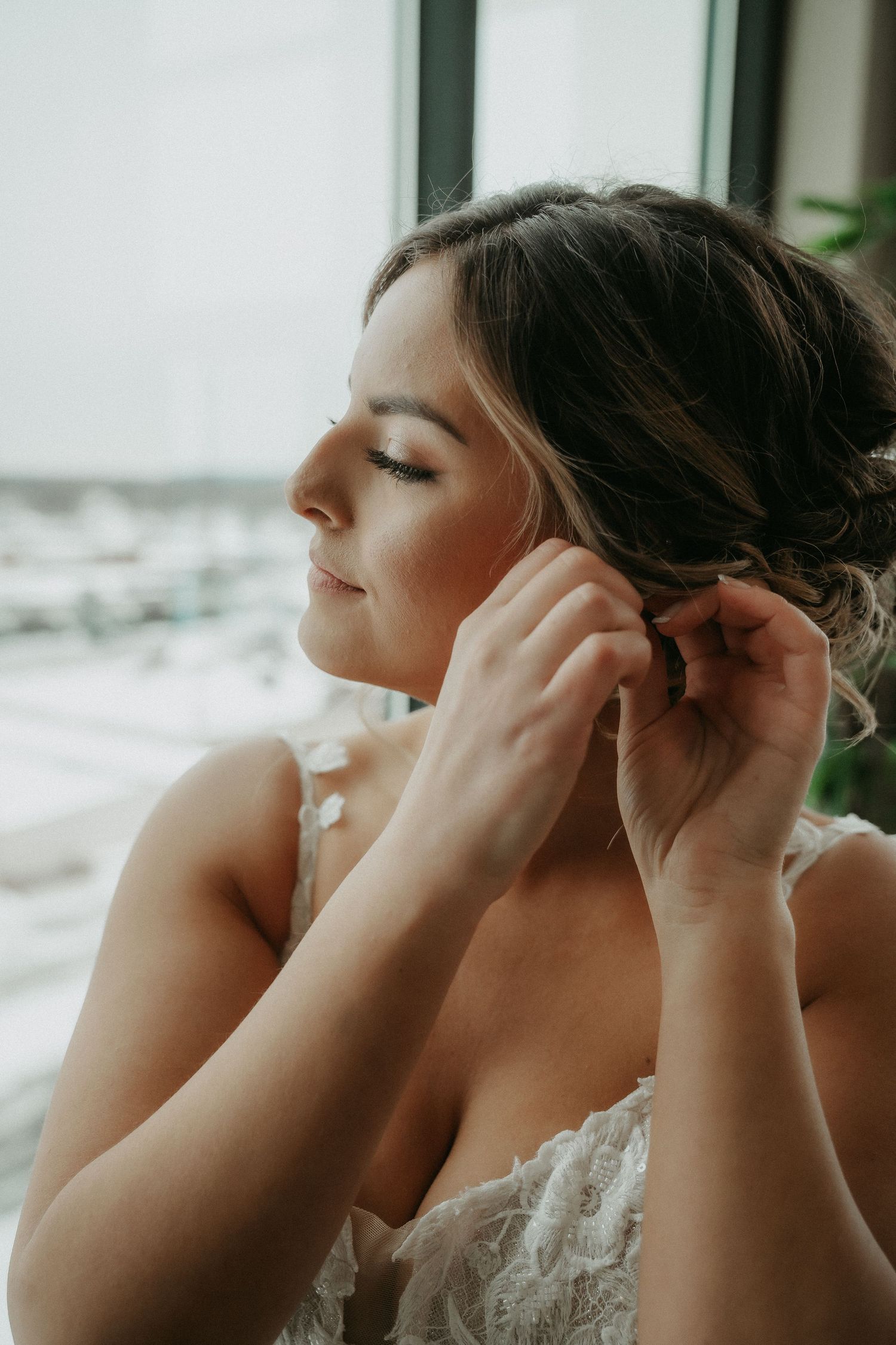A bride in a white dress puts on her earrings while getting ready for her wedding ceremony.